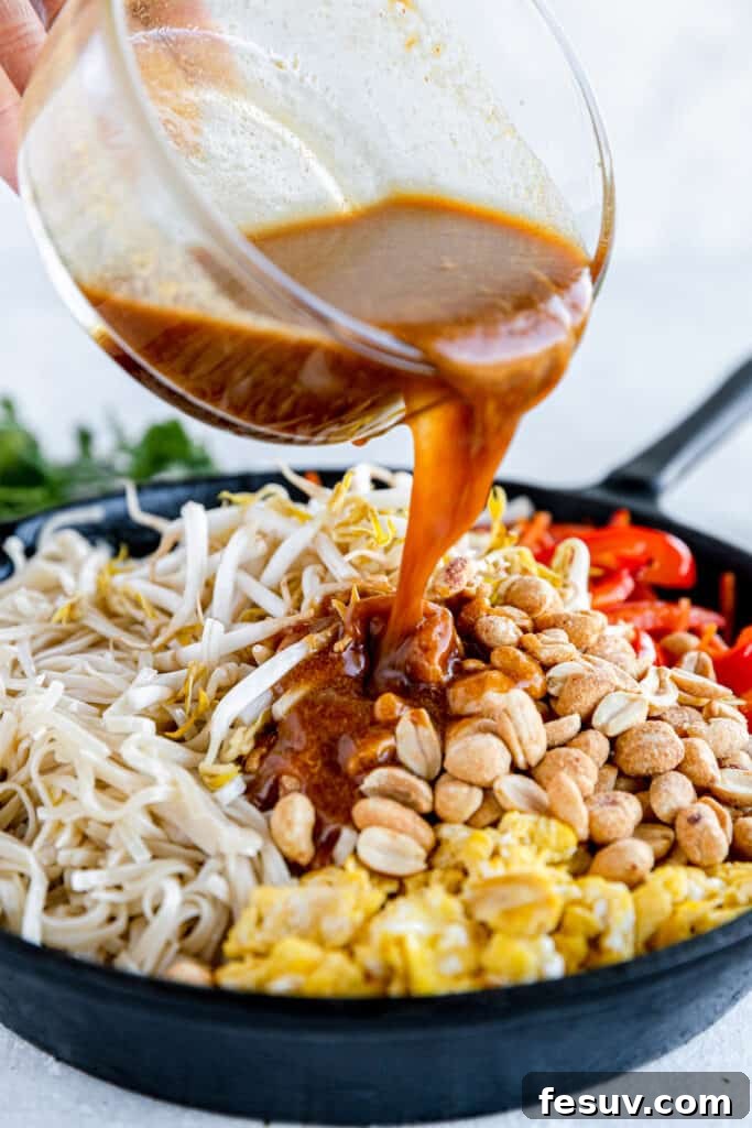 In this easy Pad Thai recipe, rice noodles are tossed with scrambled eggs, roasted peanuts, colorful veggies, and a sweet, salty, sour sauce. Pad Thai Sauce Being Poured Over the Skillet of Prepared Pad Thai