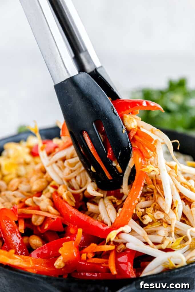 In this easy Pad Thai recipe, rice noodles are tossed with scrambled eggs, roasted peanuts, colorful veggies, and a sweet, salty, sour sauce. The Prepared Veggies and Nuts for Pad Thai Being Mixed with a Pair of Tongs
