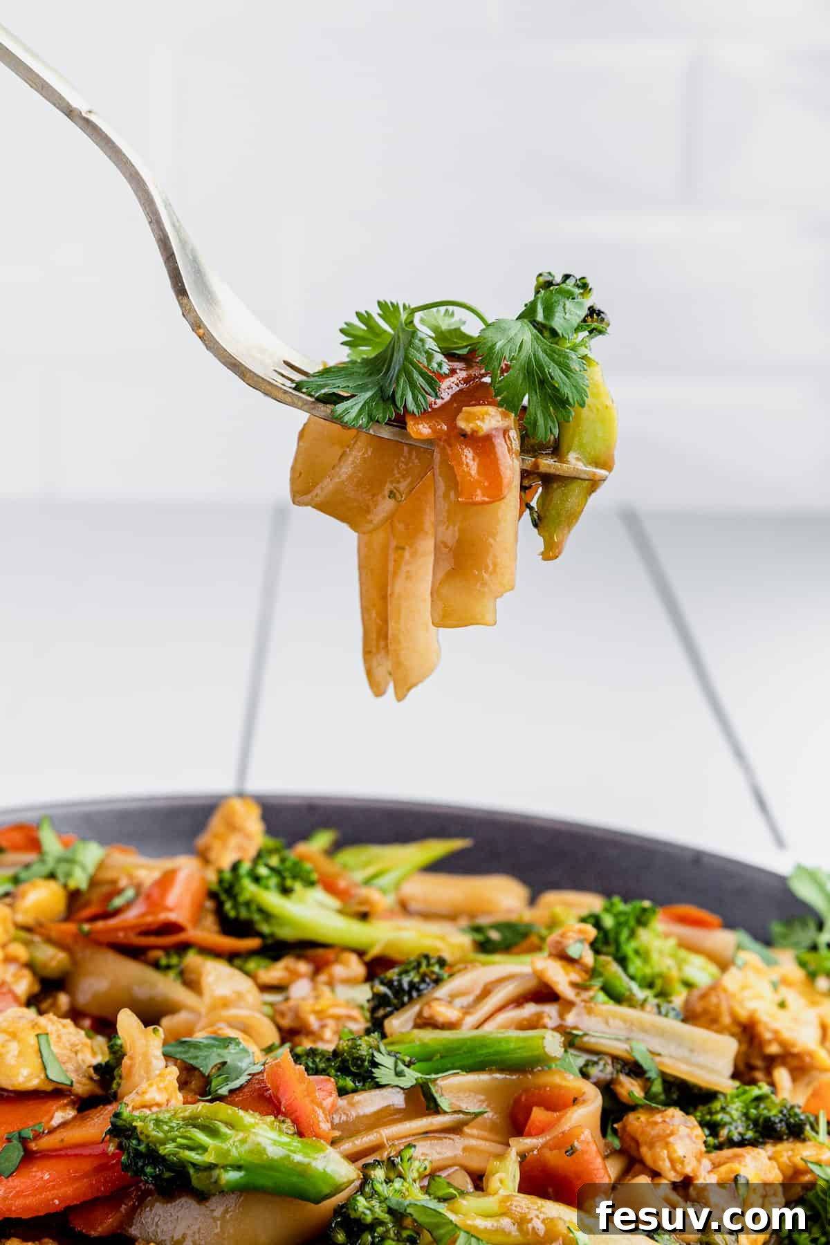 Thai Wide Noodle Perfection 3 A Bite of Pad See Ew on a Fork Hovering Above a Full Plate