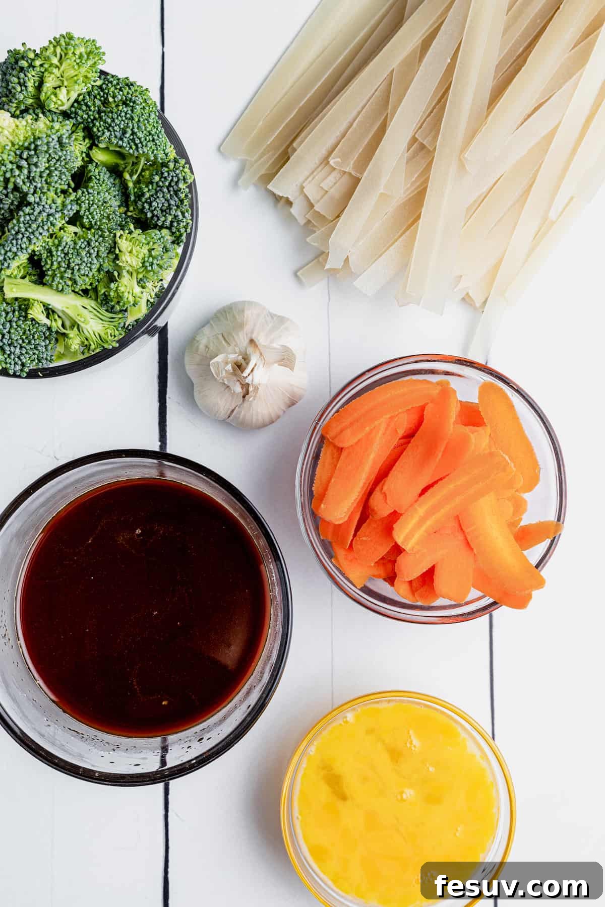 Thai Wide Noodle Perfection 5 Broccoli, Flat Rice Noodles, Carrot Slices and the Rest of the Ingredients on Top of a White Picnic Table