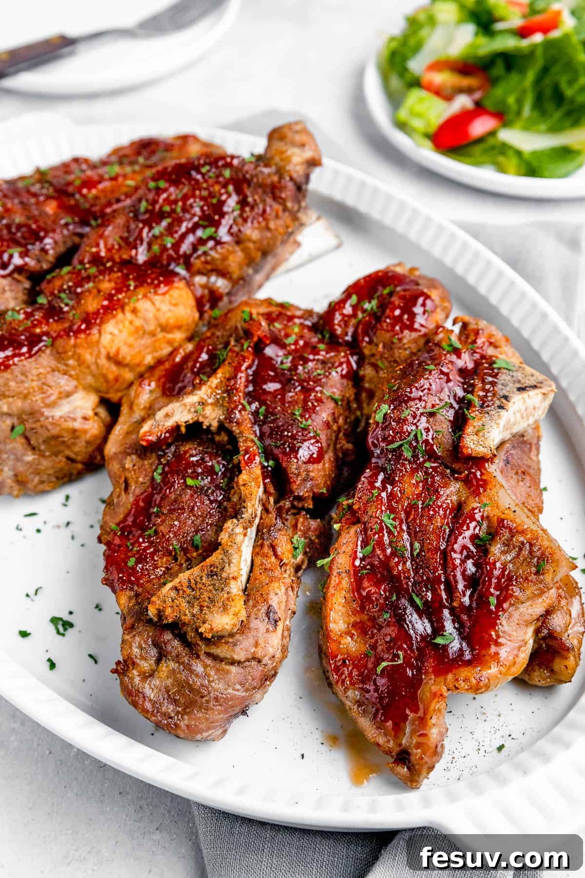 Fall-Off-The-Bone Instant Pot Ribs 6 Side shot of Instant Pot Ribs on a white serving platter with a small salad in the background, highlighting the glossy barbecue sauce