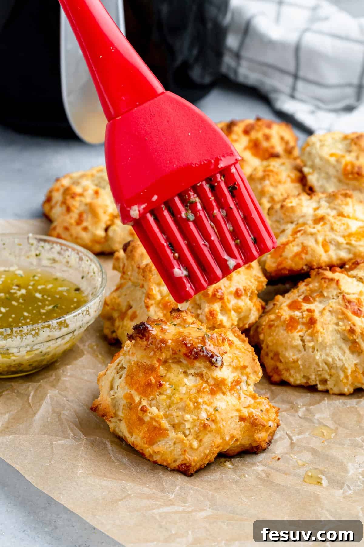 Garlic Butter Being Brushed Over an Air Fryer Biscuit with a Red Pastry Brush