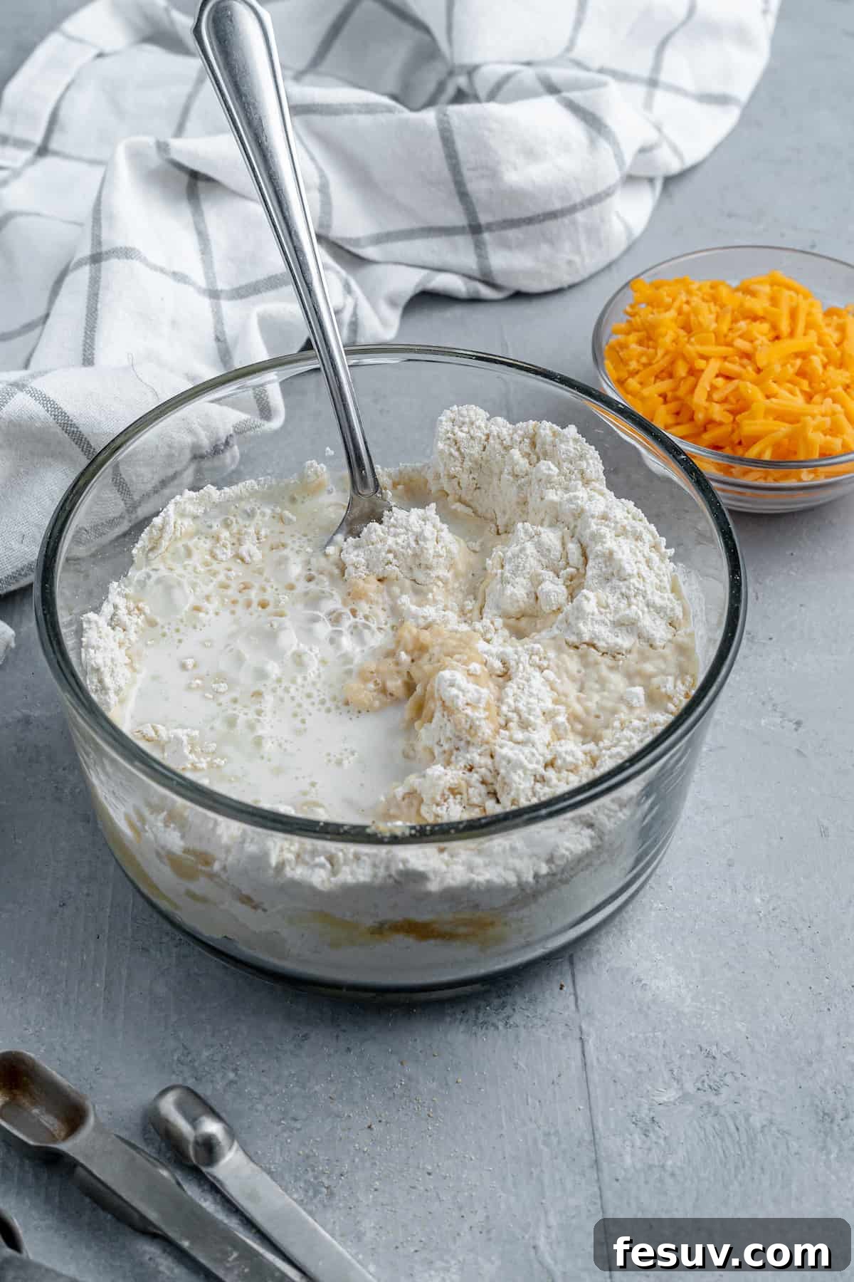 Bisquick Mix, Milk and Butter in a Bowl Beside a Dish of Shredded Cheddar