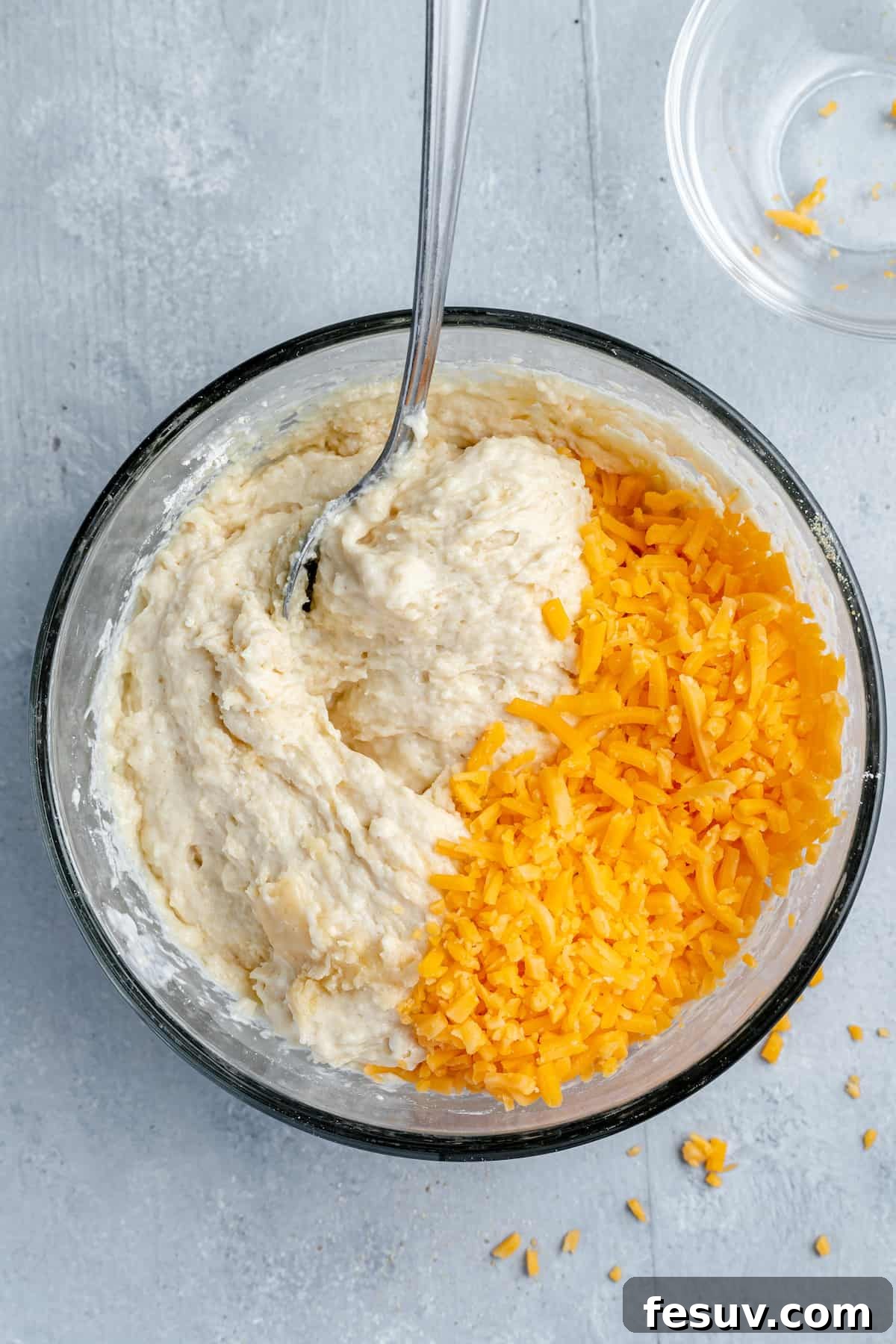 Shredded Cheddar Cheese Being Mixed Into the Biscuit Batter with a Spoon