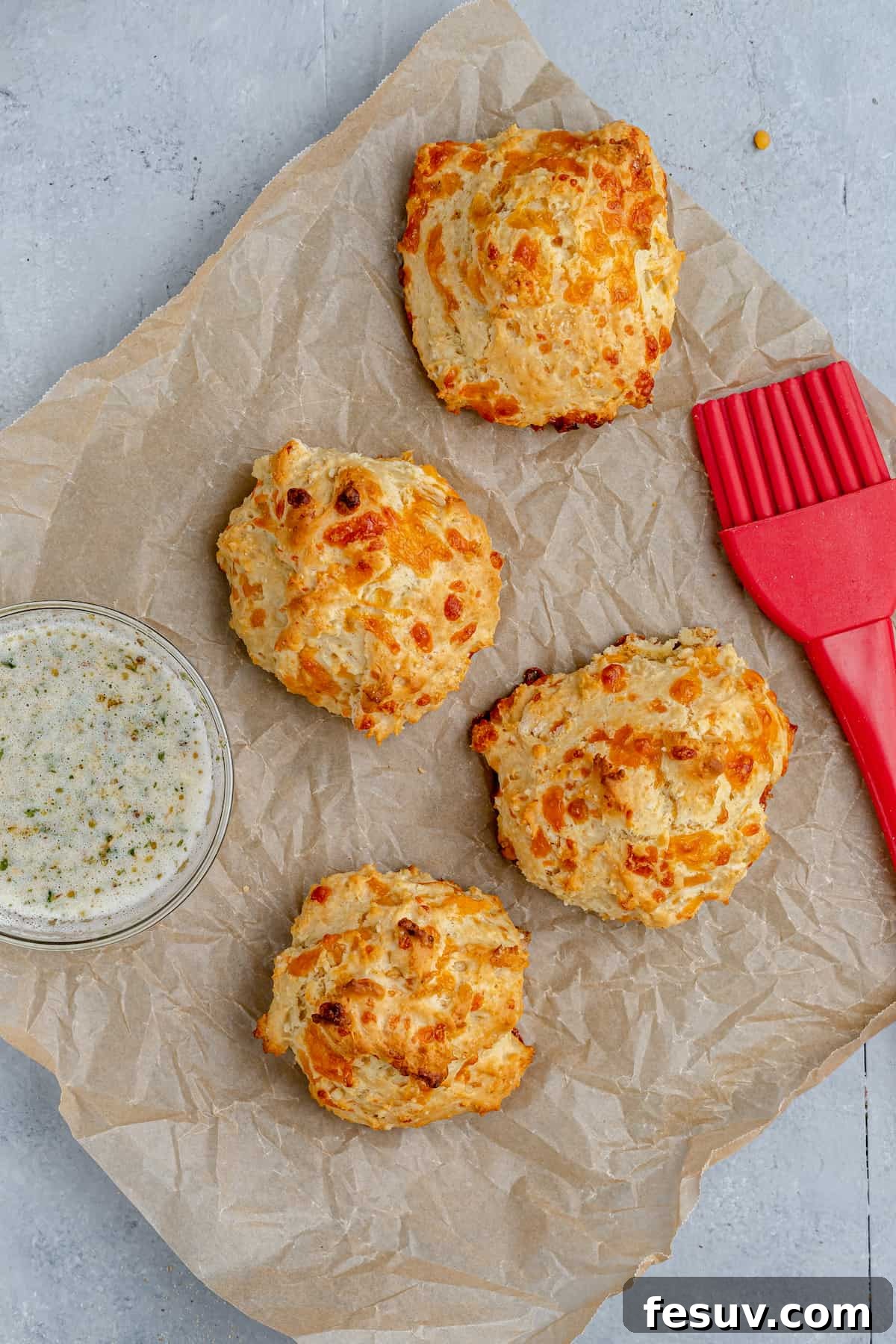 Four Air Fryer Biscuits on a Sheet of Parchment Paper with a Pastry Brush and a Small Dish of Garlic Butter