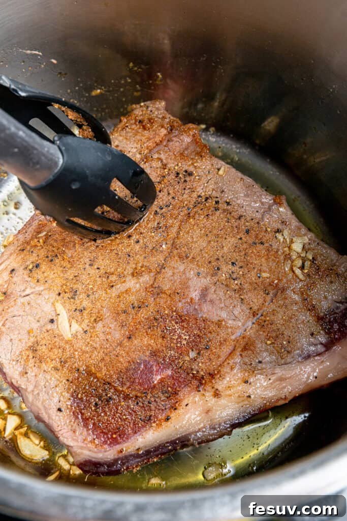 Savory Instant Pot Pot Roast with Hearty Root Vegetables 5 Tongs holding a piece of browned chuck roast, showcasing the delicious sear achieved in the Instant Pot.