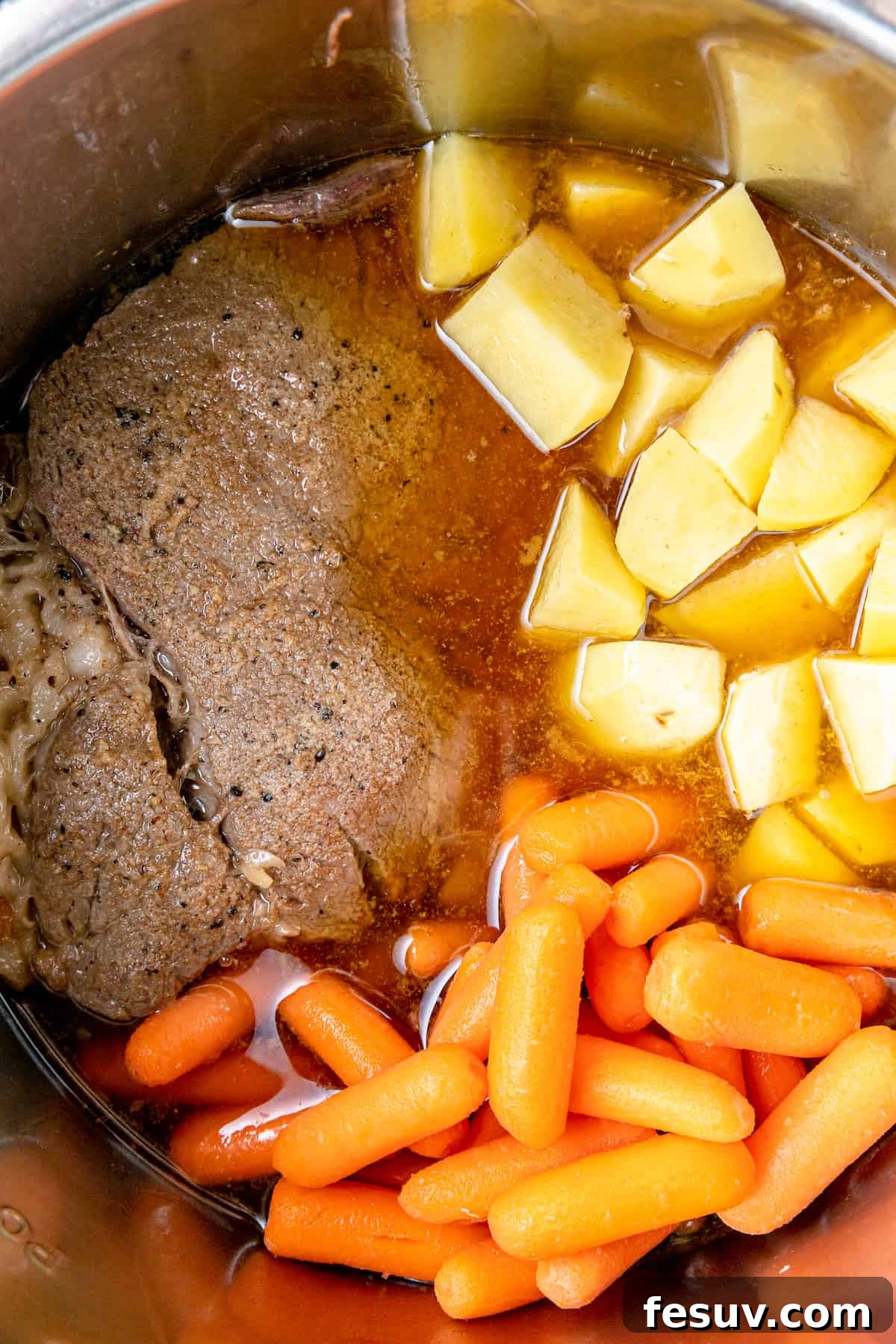 Savory Instant Pot Pot Roast with Hearty Root Vegetables 6 A large piece of browned chuck roast nestled in beef broth inside the Instant Pot, with carrots and potatoes surrounding it.