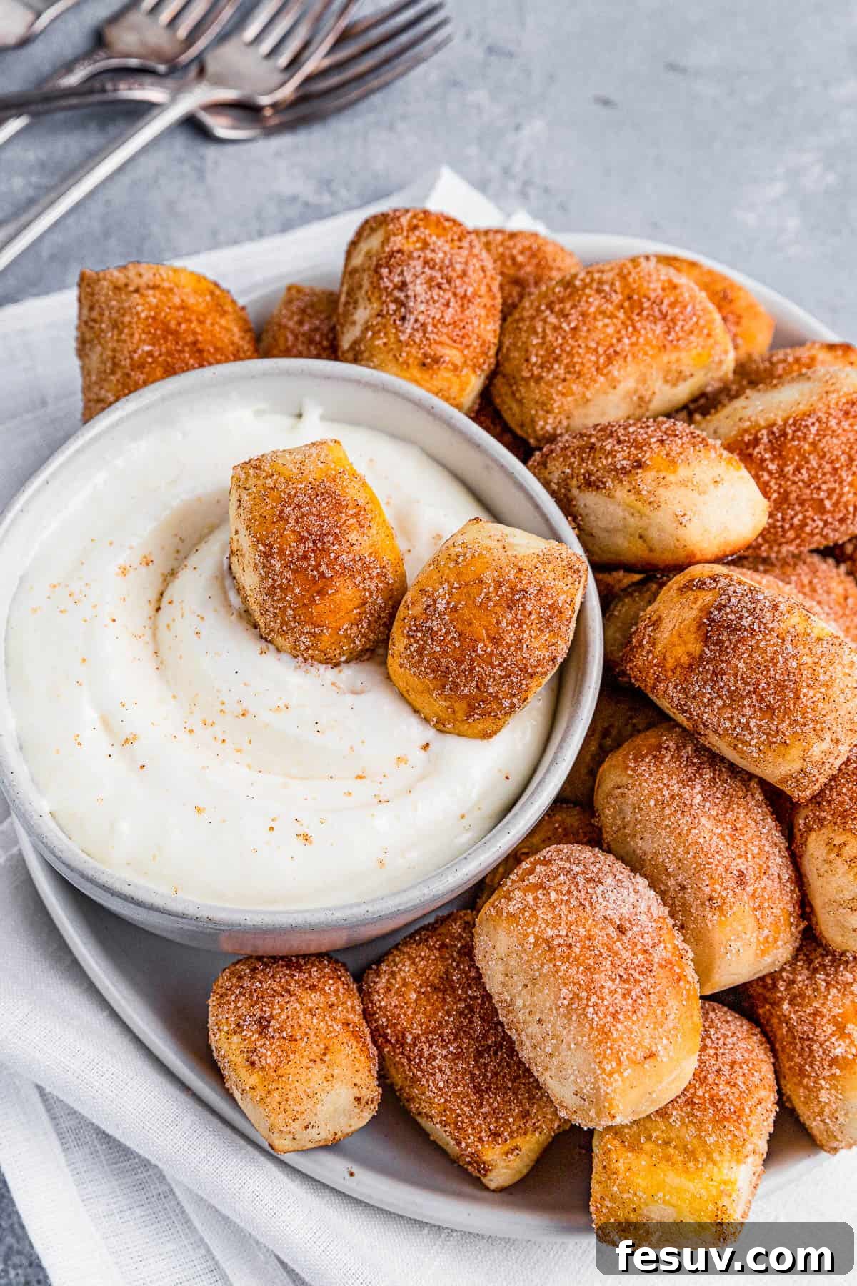 Close-up of cinnamon sugar pretzel bites being dipped into the creamy white sauce.