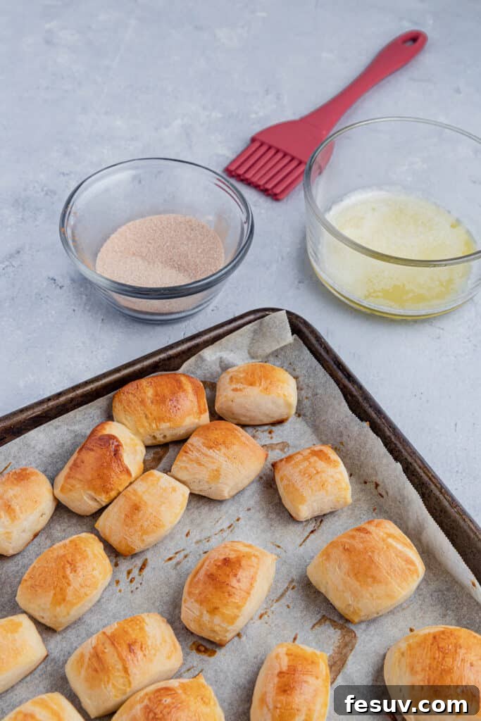 Baked pretzel bites alongside bowls of melted butter and cinnamon sugar, ready for coating.