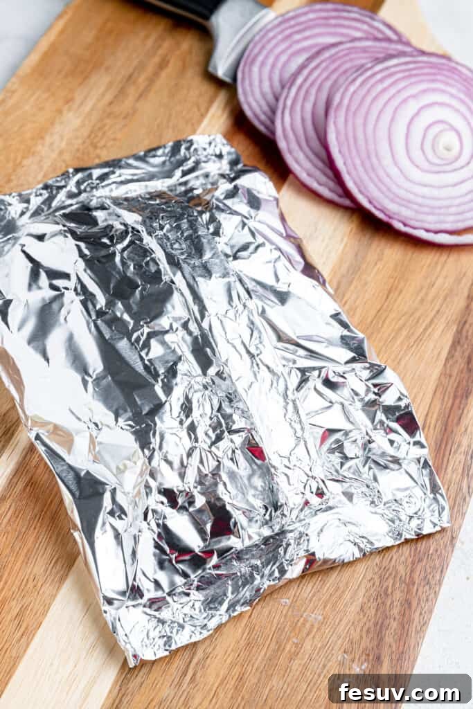 Hearty Cheeseburger Foil Packs with Potatoes and Vegetables 4 Folded foil on a cutting board and stuffed with cheeseburgers