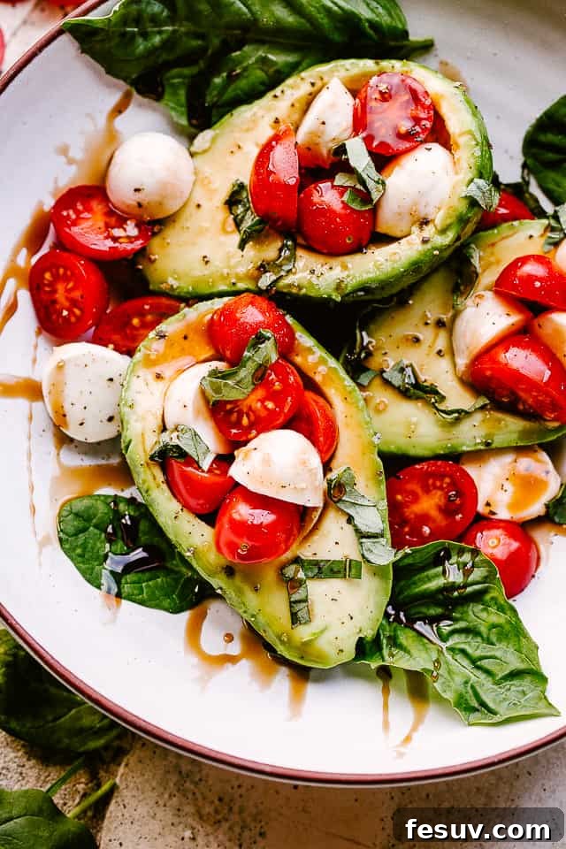 Two halves of Caprese Stuffed Avocados presented beautifully on a white plate, garnished with basil.