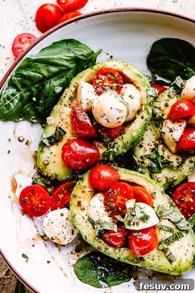 A close-up view of fresh ingredients for Caprese Stuffed Avocados, including cherry tomatoes, mozzarella balls, and basil leaves.