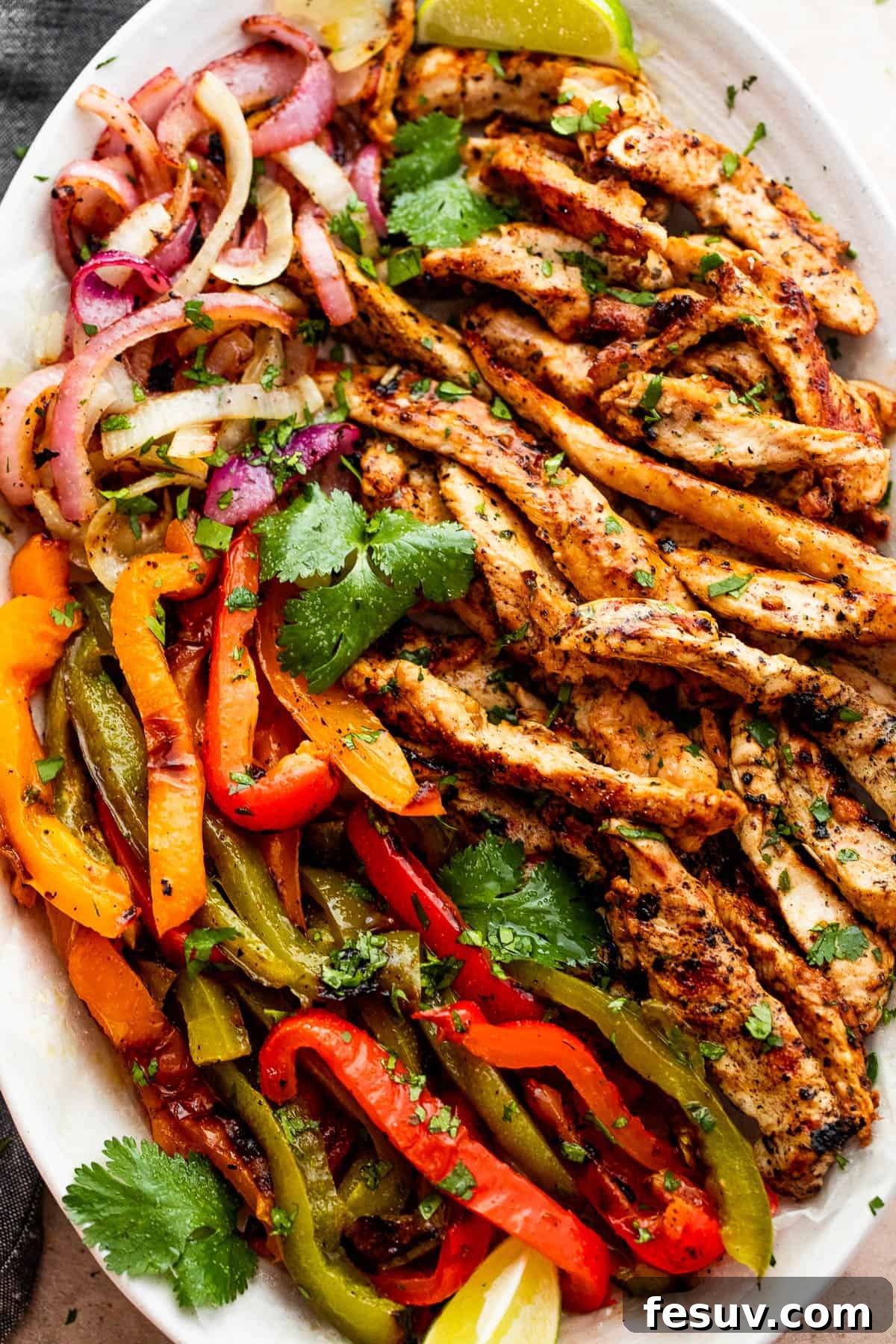 grilled chicken strips, colorful bell pepper strips, and onions on a serving plate garnished with cilantro leaves