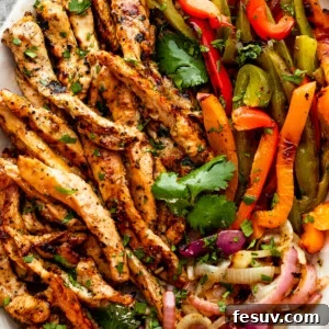 grilled chicken fajitas with chicken strips, colorful bell pepper strips, and onions on a serving plate garnished with cilantro leaves