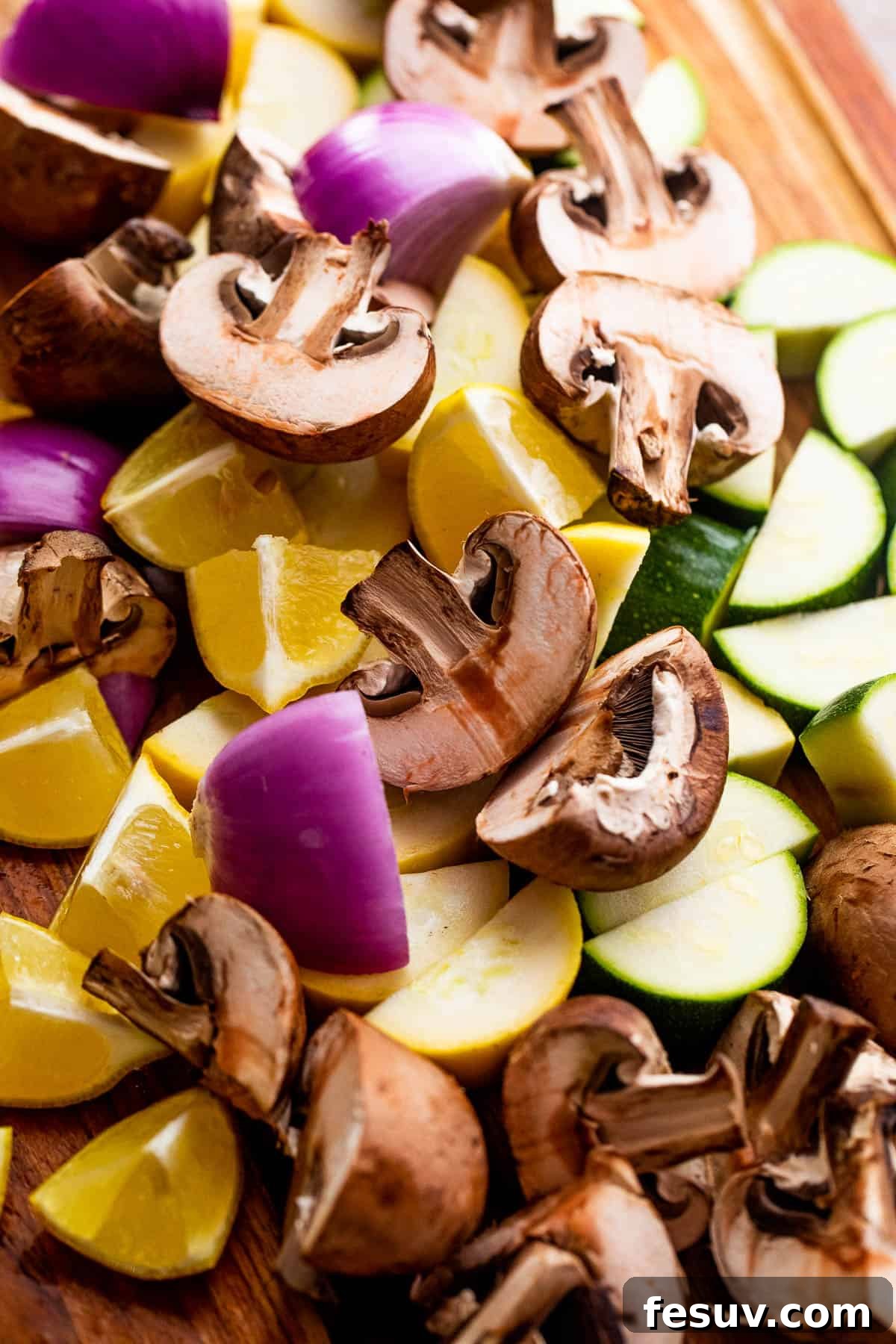 Garden Fresh Grilled Squash Skewers 3 A vibrant assortment of chopped mushrooms, red onions, lemons, zucchini, and yellow squash arranged on a rustic wooden board, ready for skewering.