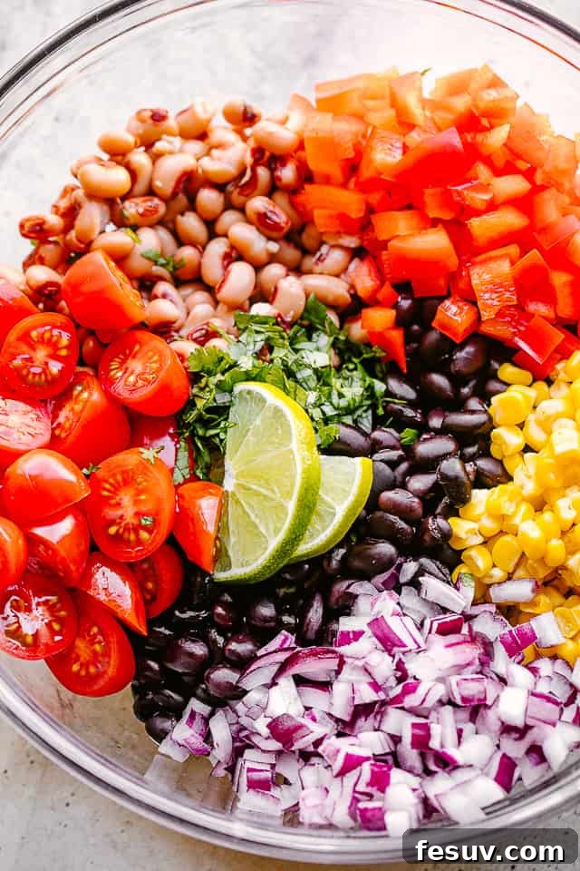 Avocado, corn, tomatoes, black-eyed peas, beans, and cilantro in a large glass bowl, ready to be mixed