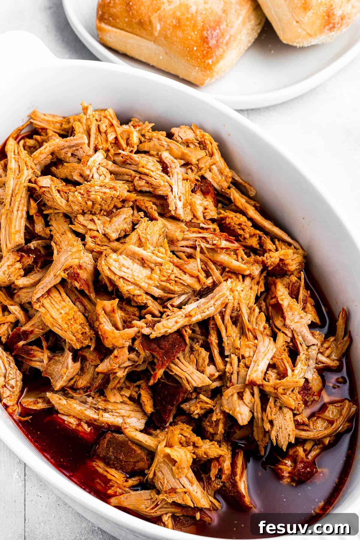 Effortless Instant Pot Pulled Pork with Zesty Coleslaw 6 Close-up of shredded pulled pork soaking in savory juices and barbecue sauce in a white baking dish