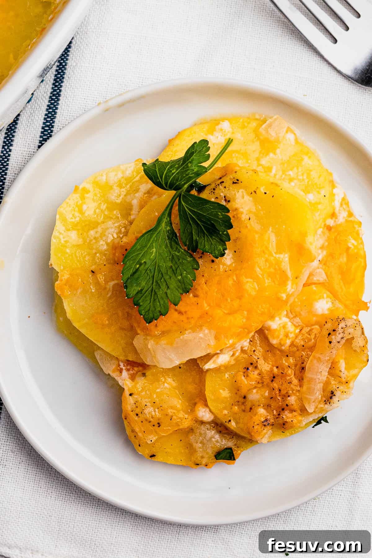 Tender sliced potatoes layered with cheddar cheese and diced onions to make a scalloped potatoes casserole. A small dish with a serving of cheesy sliced potatoes, perfectly golden and creamy.