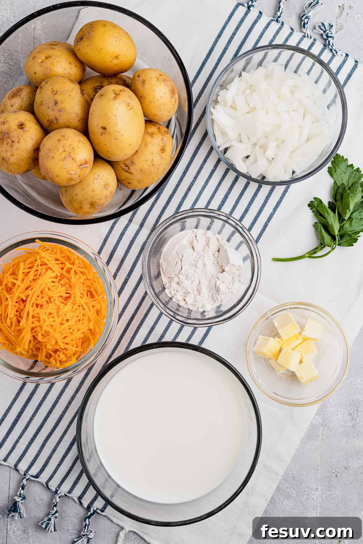 Tender sliced potatoes layered with cheddar cheese and diced onions to make a scalloped potatoes casserole. Clockwise from the top: diced onion, all-purpose flour, cubed butter, evaporated milk, shredded cheddar cheese, whole washed potatoes, all key ingredients for scalloped potatoes.