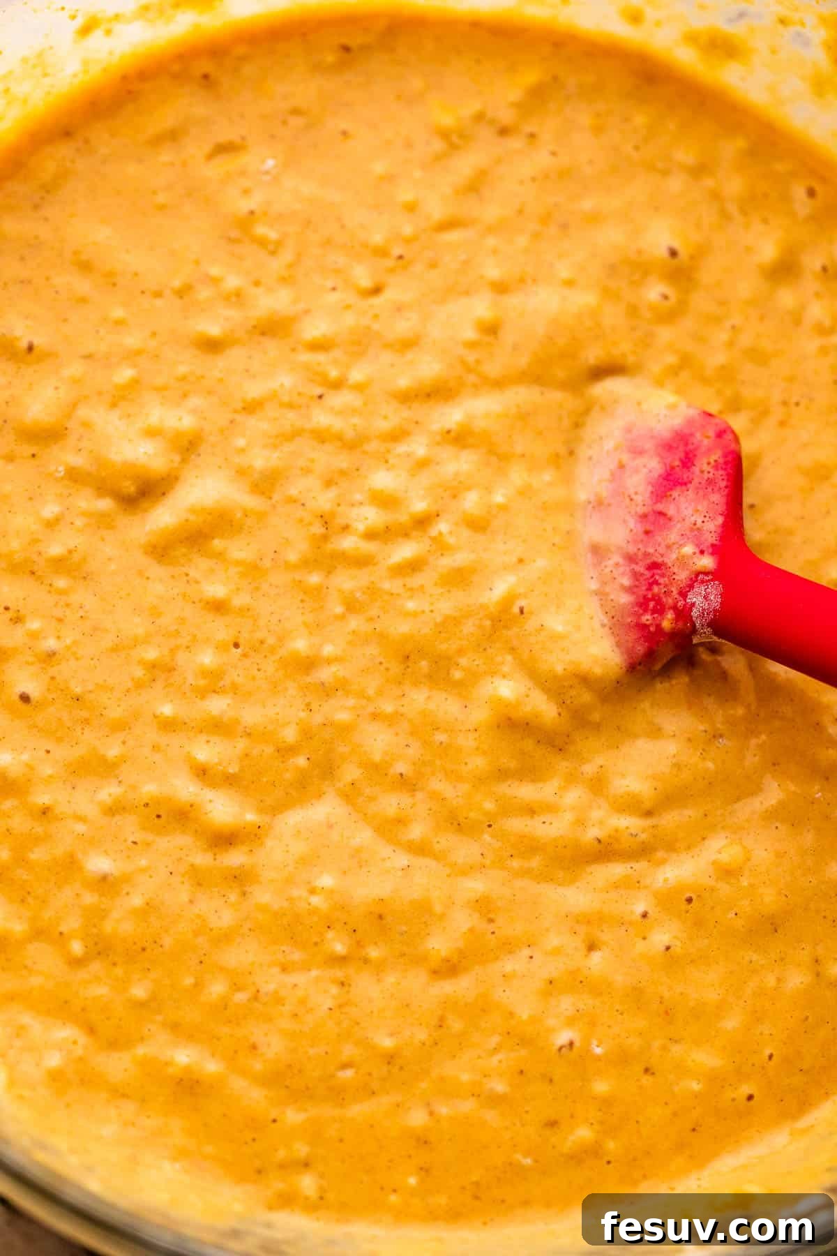 A bowl of pumpkin pancake batter being gently stirred with a whisk, showcasing its smooth, creamy texture and vibrant orange color before baking.