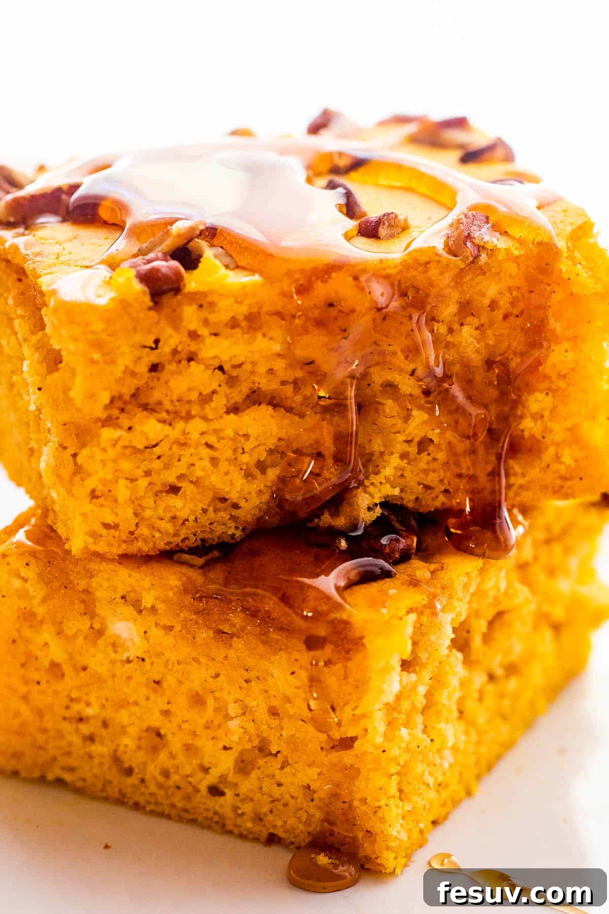 Two beautifully baked sheet pan pumpkin pancakes, perfectly square and fluffy, stacked one on top of the other, with a gentle drizzle of maple syrup.