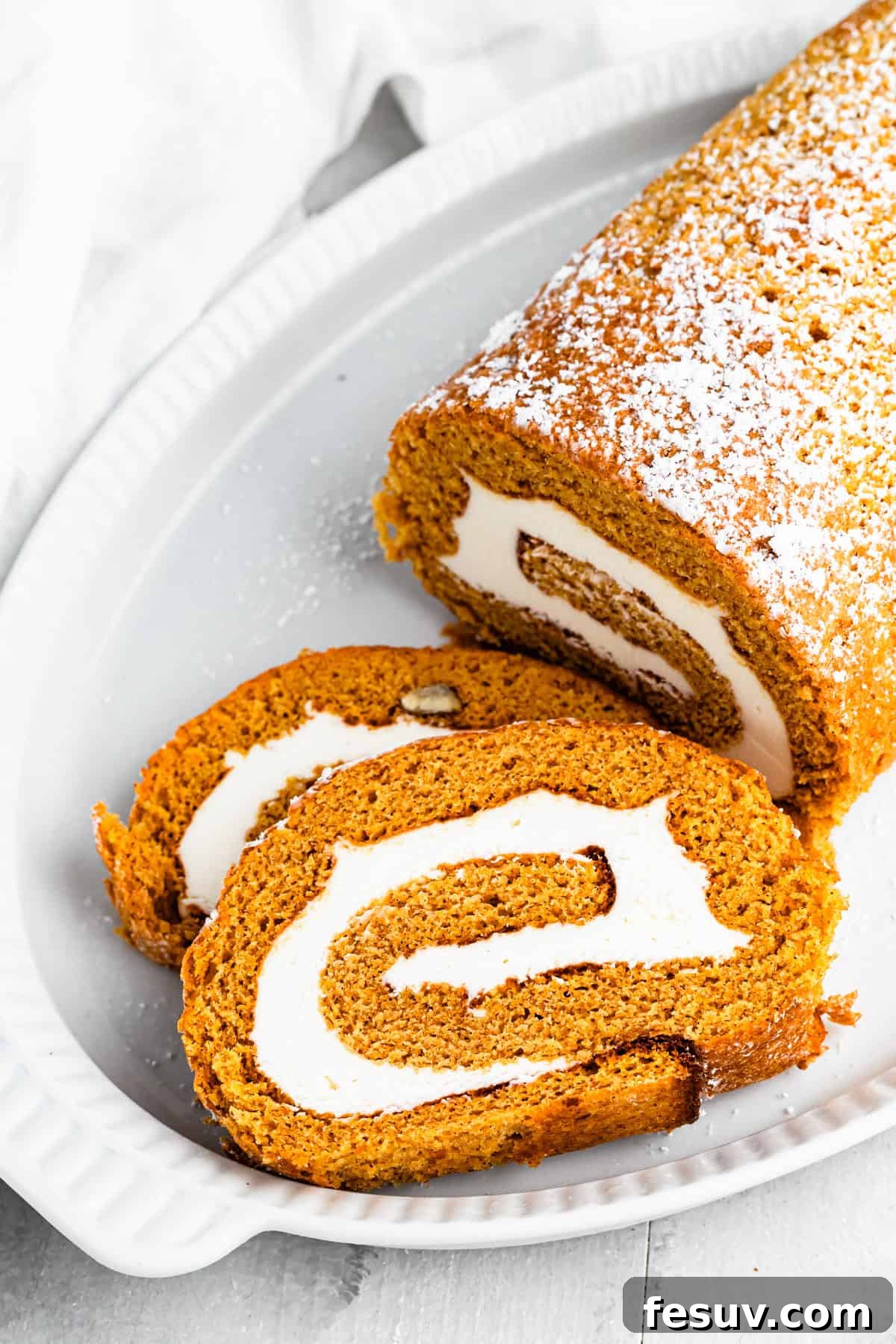 A pumpkin roll served on a plate with one slice cut out.