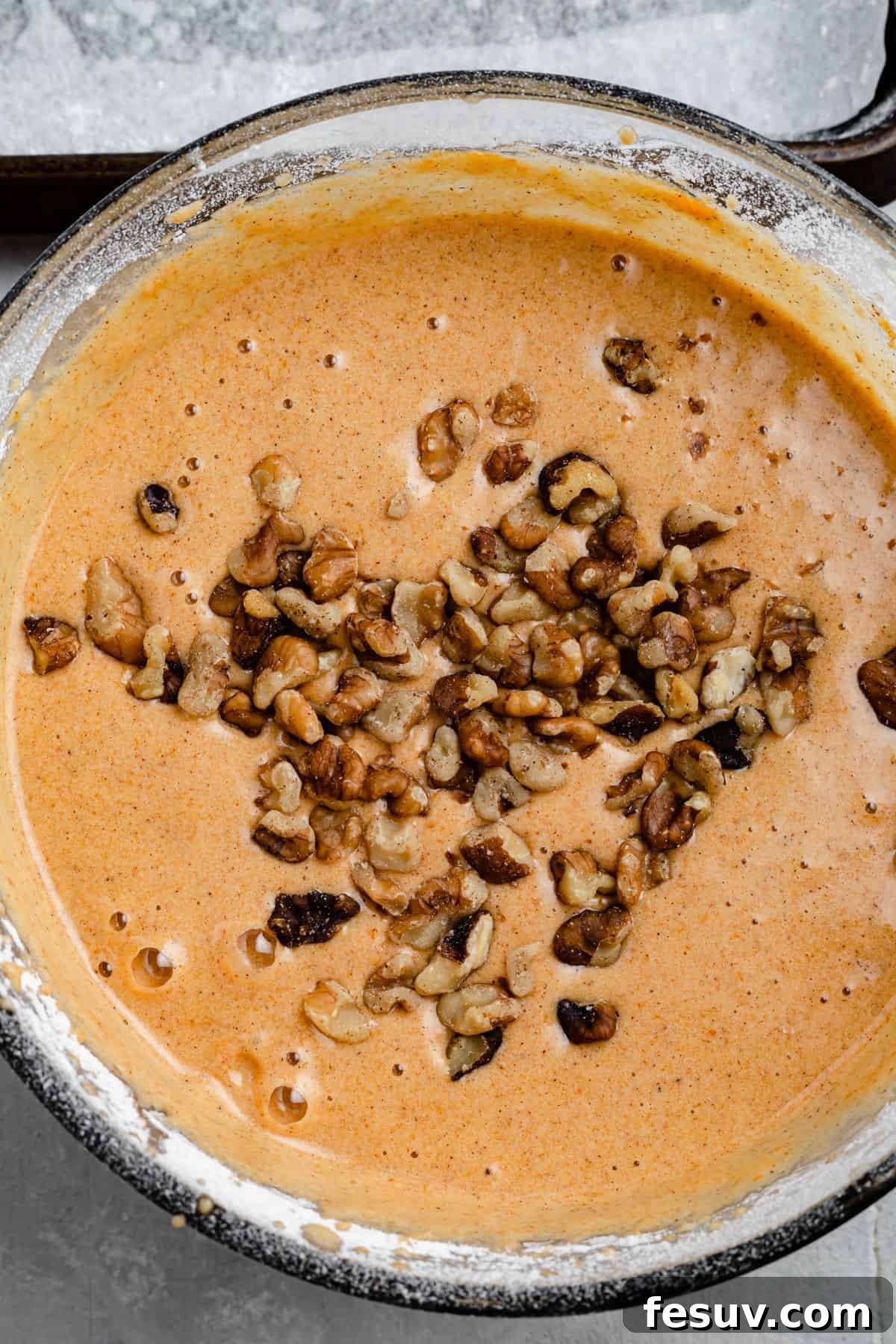 A mixing bowl full of pumpkin cake batter, with chopped walnuts sprinkled on the surface of the batter.