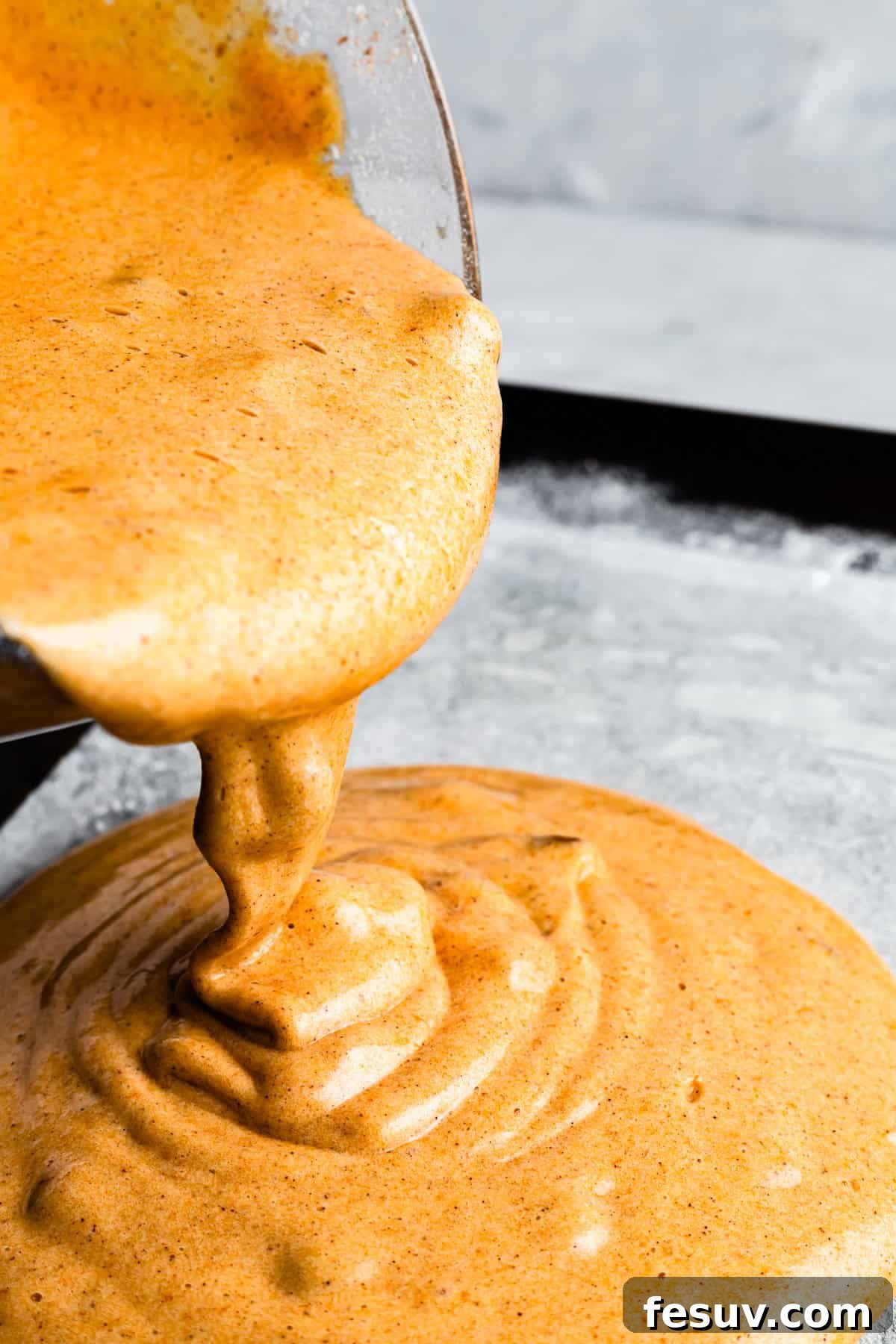 Pouring cake batter into a parchment paper-lined baking sheet.