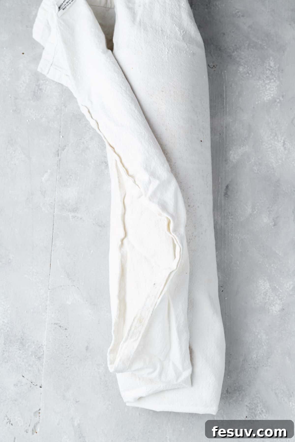 The pumpkin roll cake rolled up tightly in a linen tea towel.