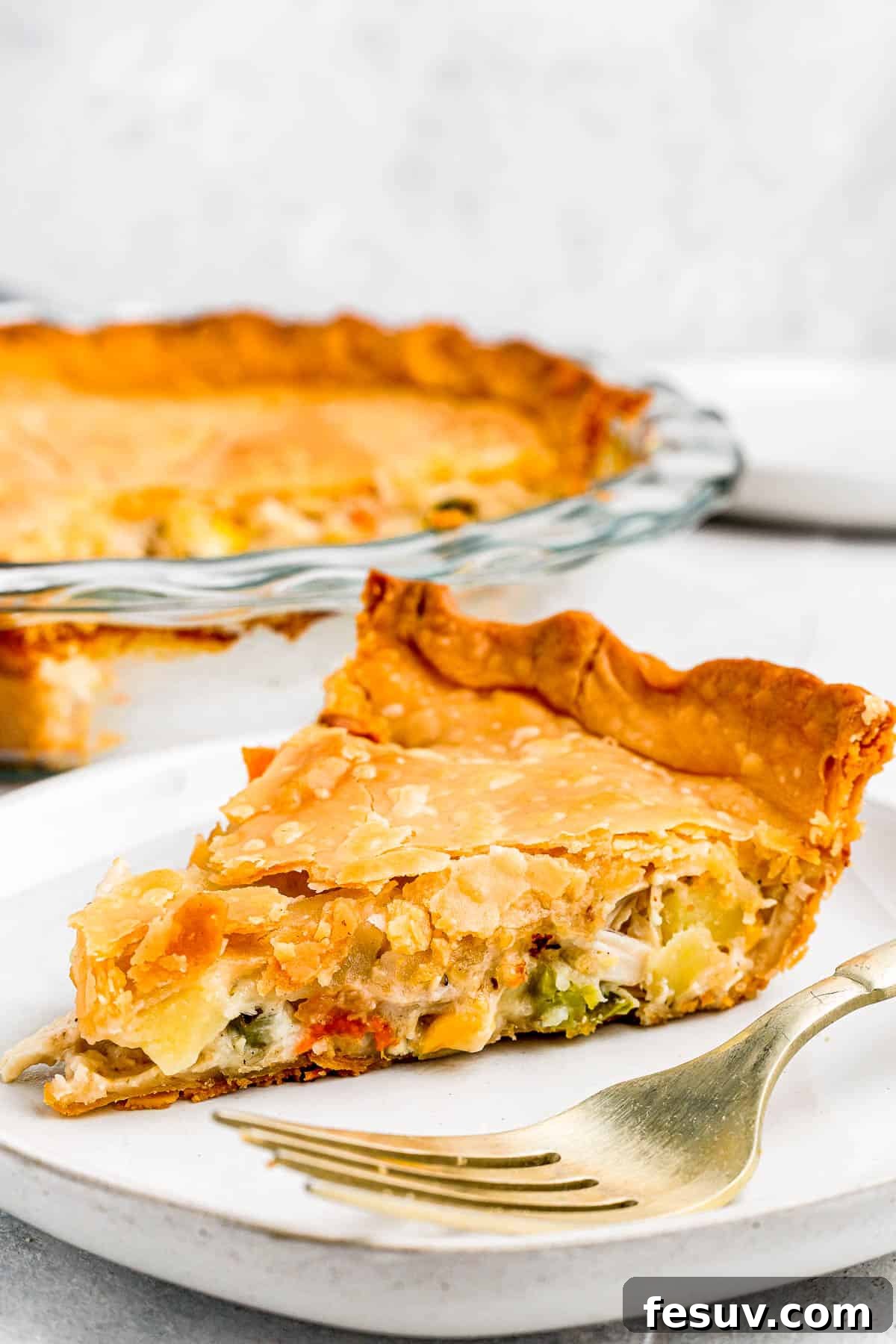 A beautifully baked chicken pot pie, golden brown and steaming, with a slice served on a plate alongside a fork, ready to be enjoyed.