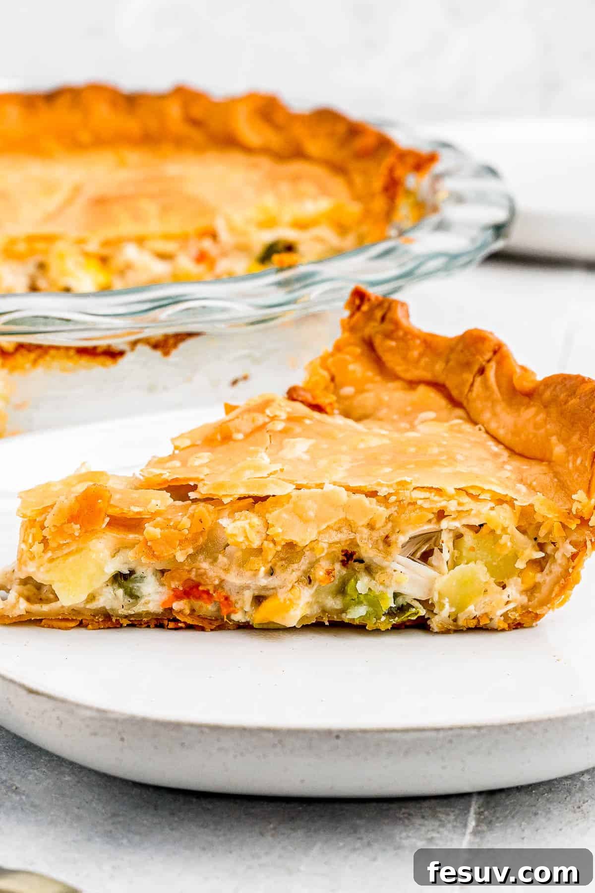 A freshly baked chicken pot pie, golden brown and inviting, with a perfectly cut slice on a white plate accompanied by a fork, ready to be enjoyed as a comforting meal.
