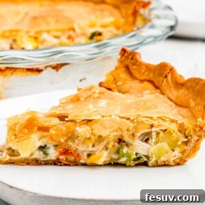 A beautifully baked chicken pot pie, golden brown and steaming, with a slice served on a plate alongside a fork.