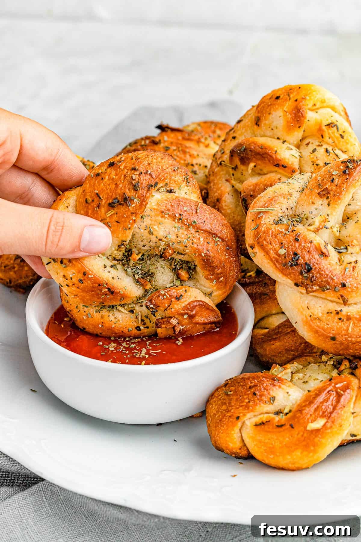Dipping a golden-brown garlic knot into a vibrant marinara sauce, highlighting its soft texture and herbed butter glaze.