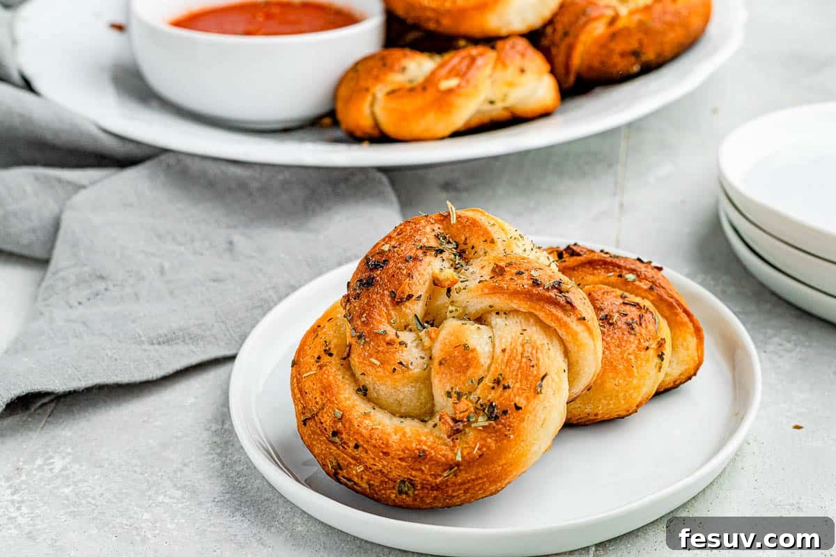A generous pile of freshly baked garlic knots arranged on a rustic plate, with a small bowl of marinara dipping sauce placed invitingly beside them.