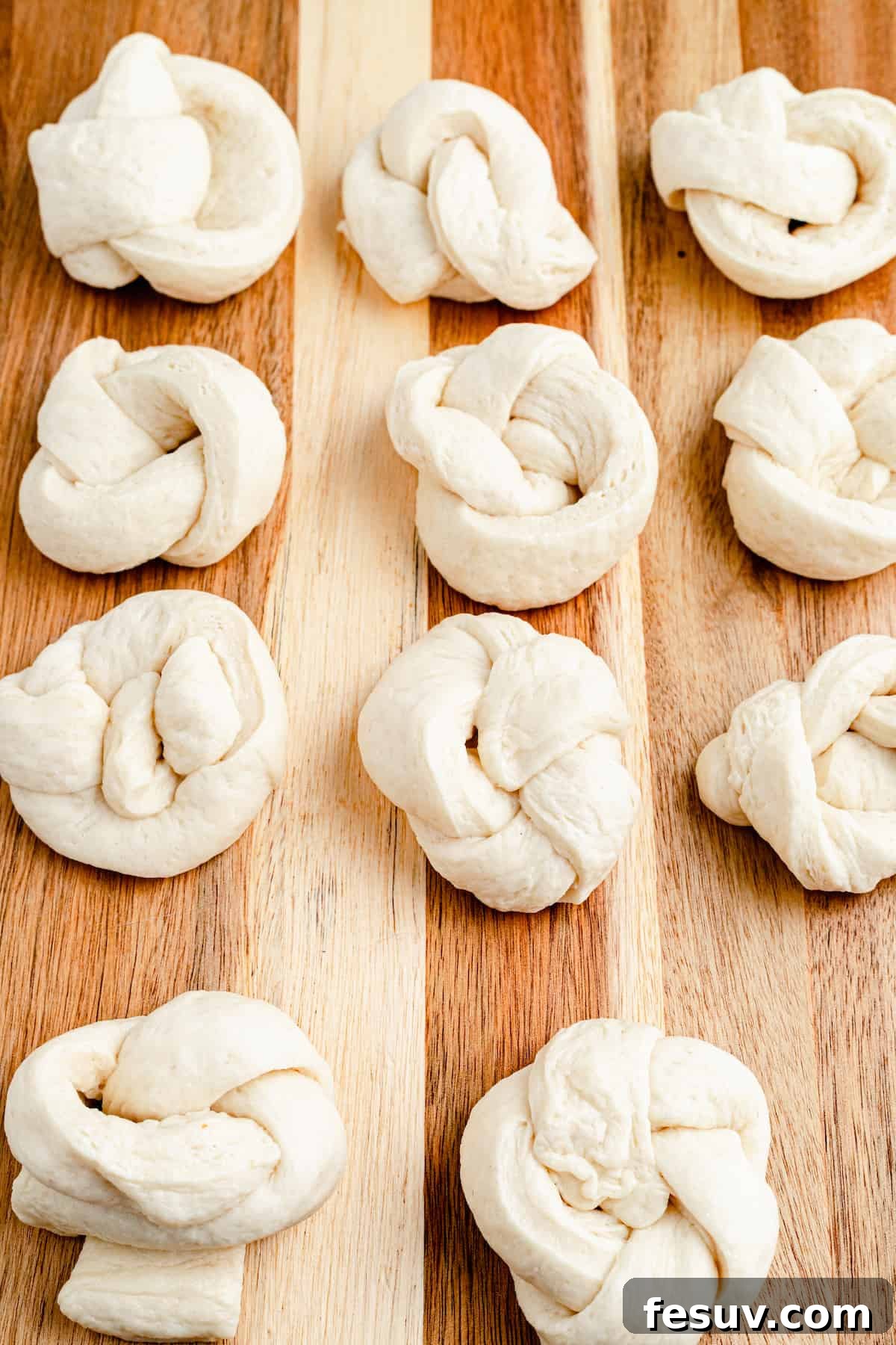 Strips of unbaked pizza dough, neatly tied into knot shapes, arranged on a lightly floured cutting board, ready for seasoning and baking.