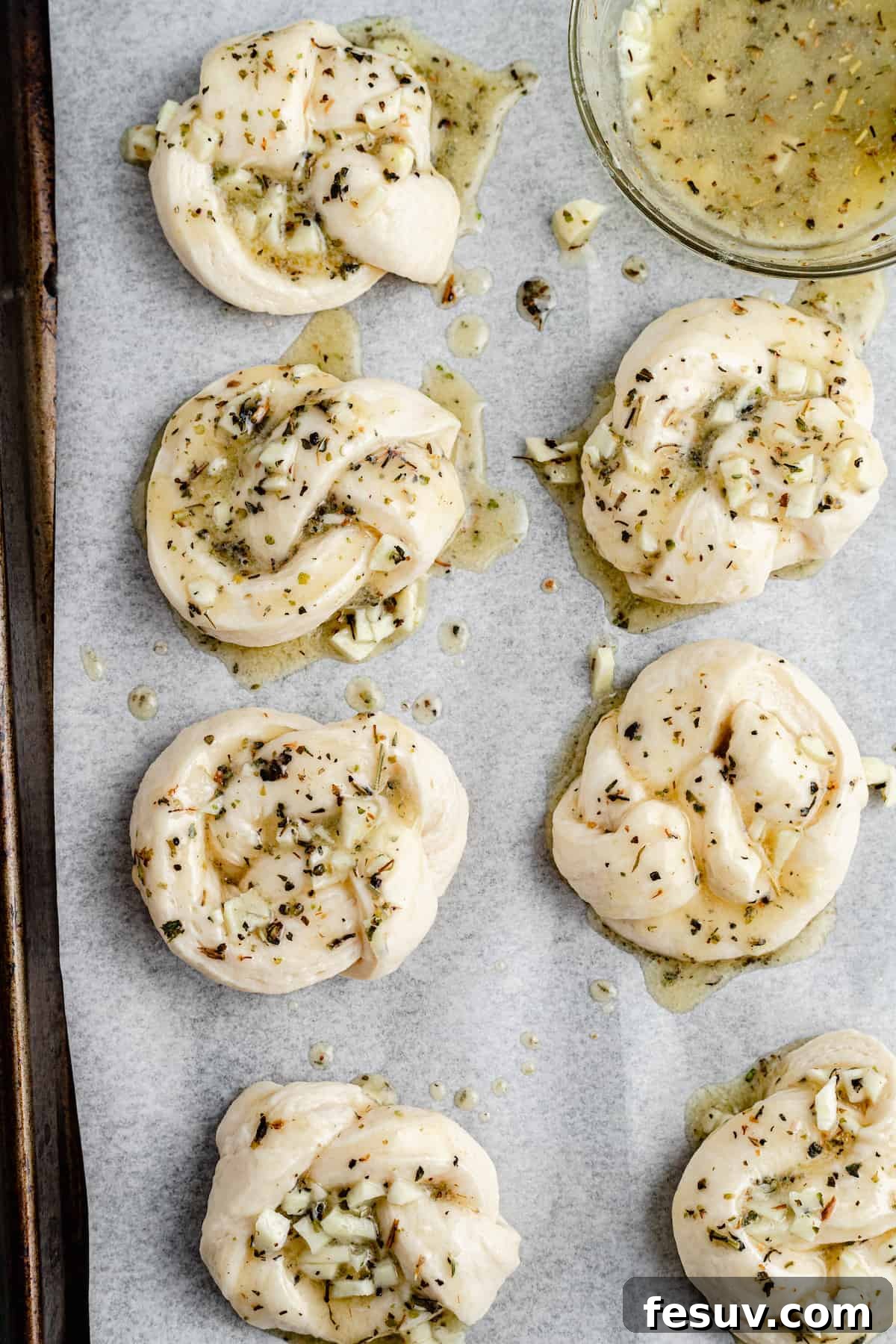 Unbaked garlic knots, beautifully arranged on a parchment-lined baking tray, each generously brushed with herbed garlic butter and ready for the oven.