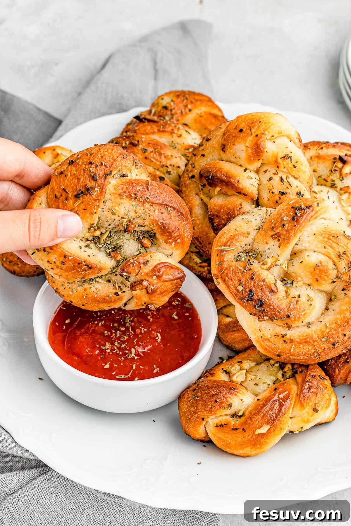 A close-up shot of a garlic knot being dipped into marinara sauce, emphasizing its soft, airy interior and golden, buttery crust.