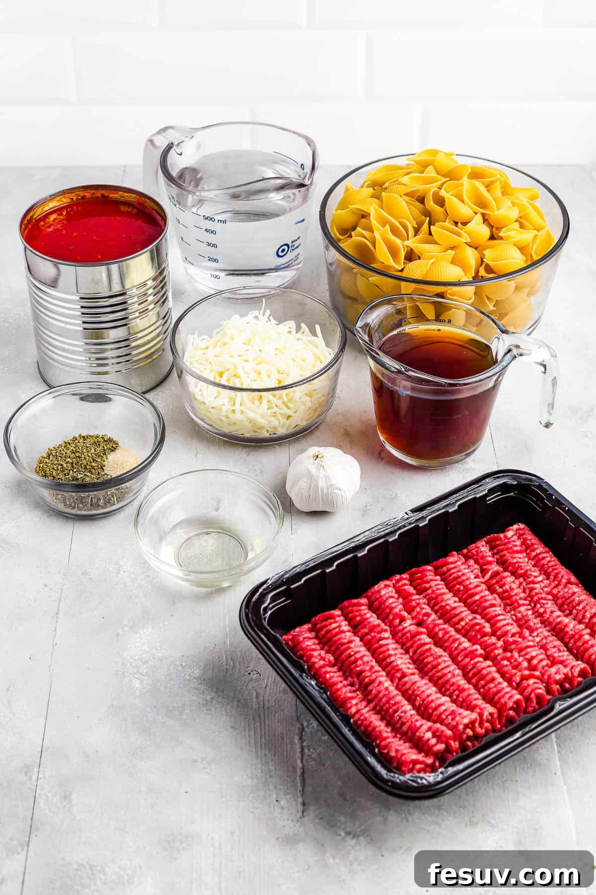 A selection of ingredients for Instant Pot Pasta Shells and Beef, including water, dry pasta, beef broth, garlic, ground beef, olive oil, seasonings, and canned tomatoes.
