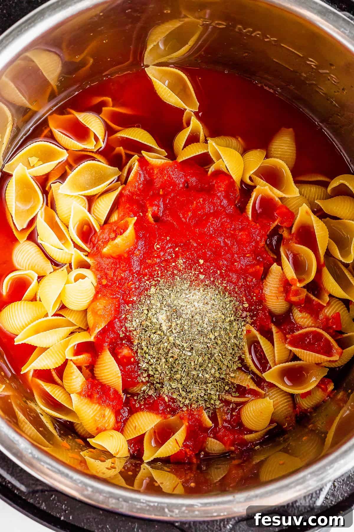 An overhead shot of an Instant Pot with crushed tomatoes, water, pasta, and seasonings inside, before cooking.