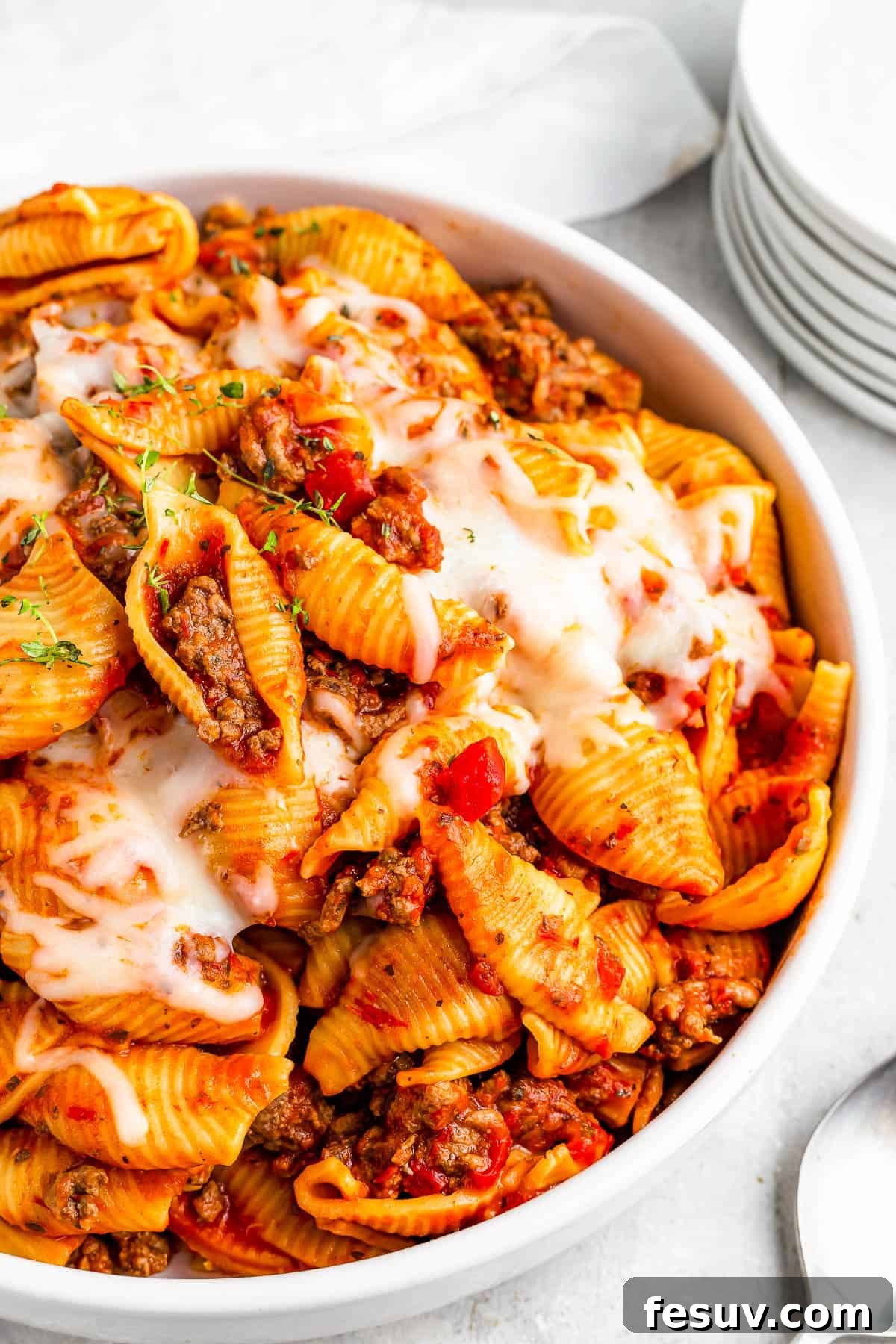 A close-up of a serving of Instant Pot pasta shells and beef in tomato sauce, topped with melted mozzarella, with fresh basil garnish.