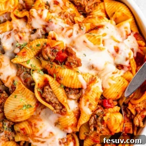 A serving dish filled with cooked pasta shells and ground beef in tomato sauce, topped with melted mozzarella.
