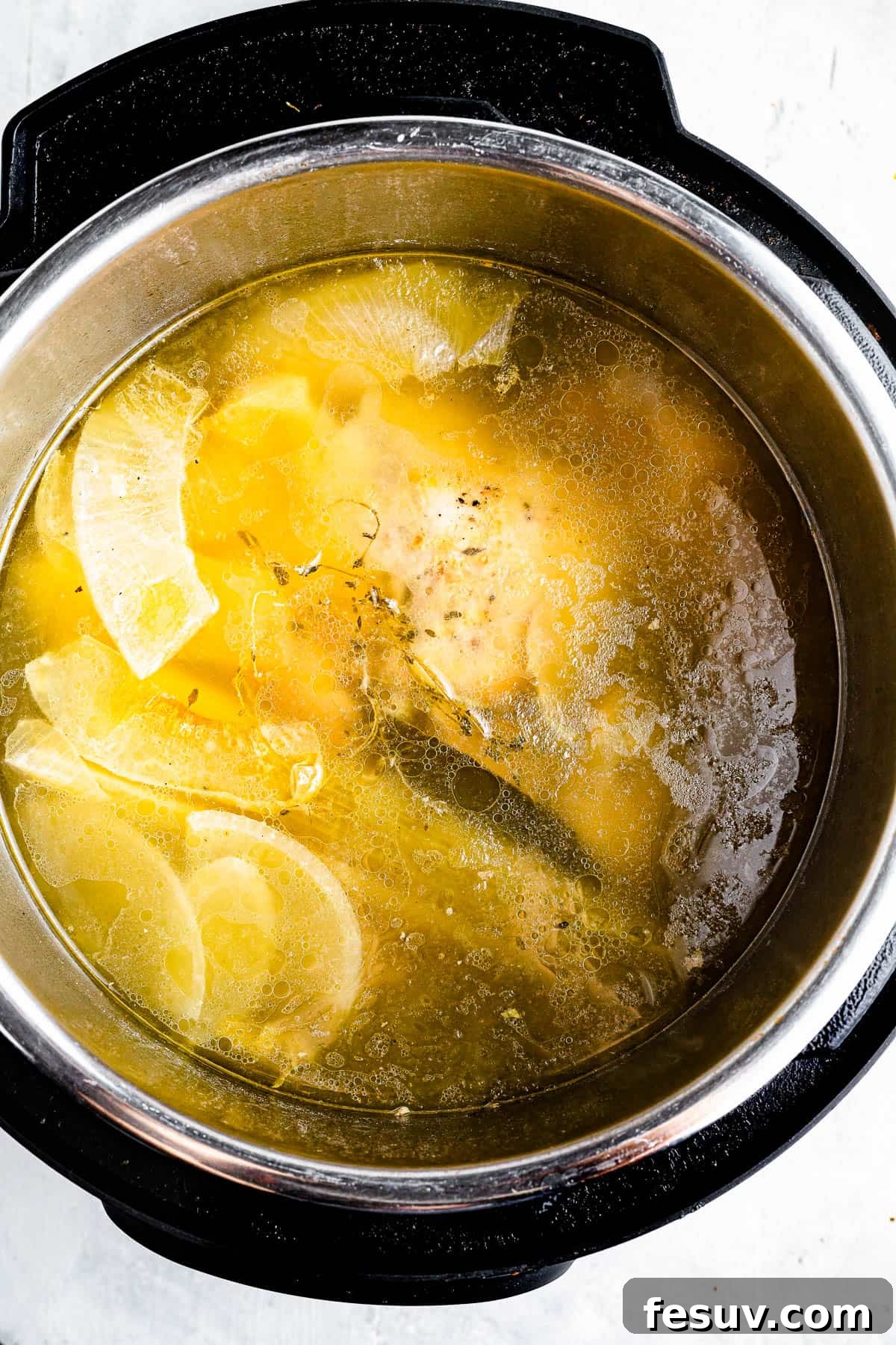 Homemade Instant Pot Chicken Broth 5 An overhead shot of the interior of an Instant Pot, filled with chicken broth, a cooked chicken, and scraps of vegetables, ready for straining.