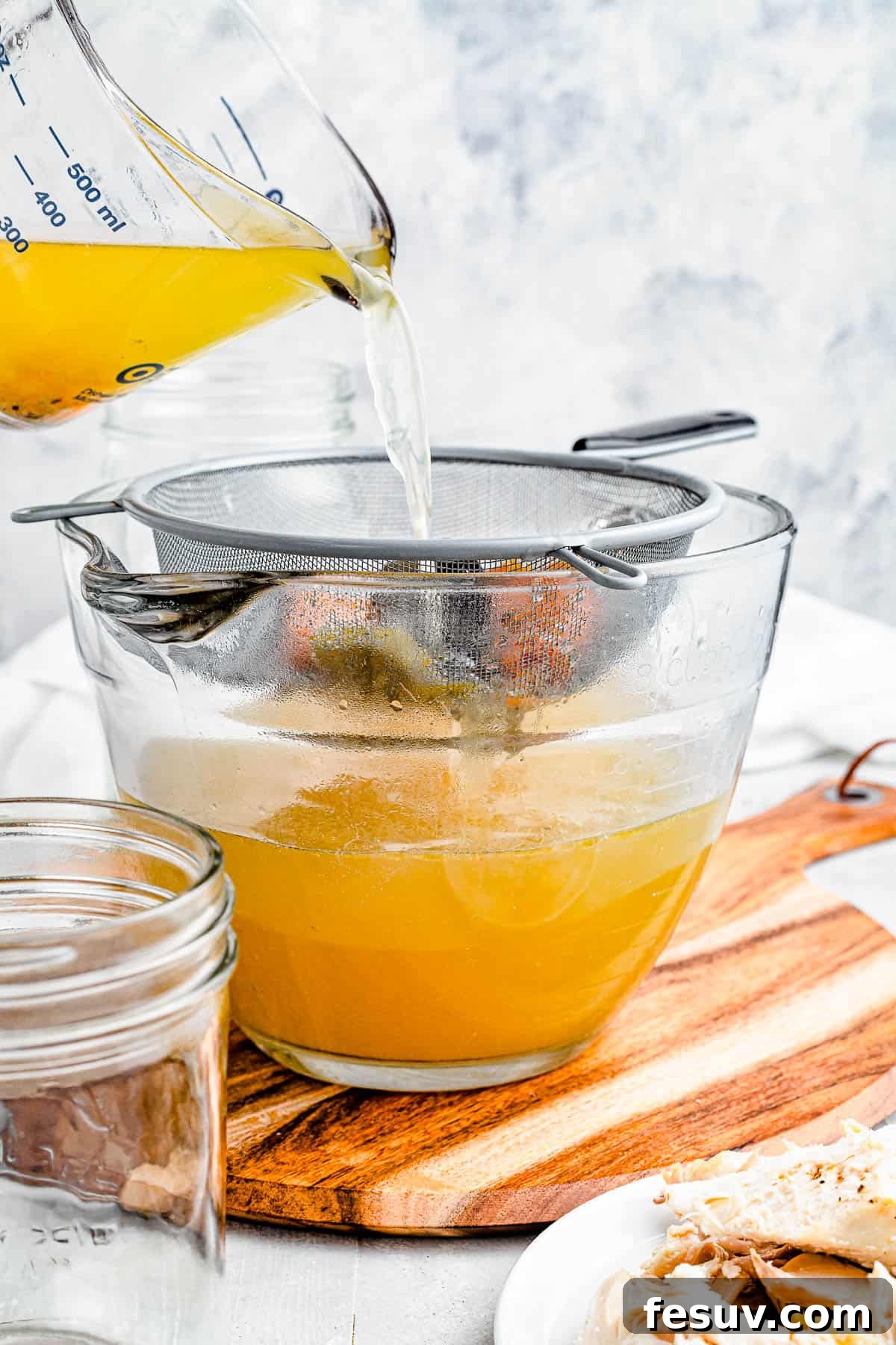Homemade Instant Pot Chicken Broth 6 Chicken broth being poured from a large measuring cup into a bowl through a large sieve, demonstrating the straining process.