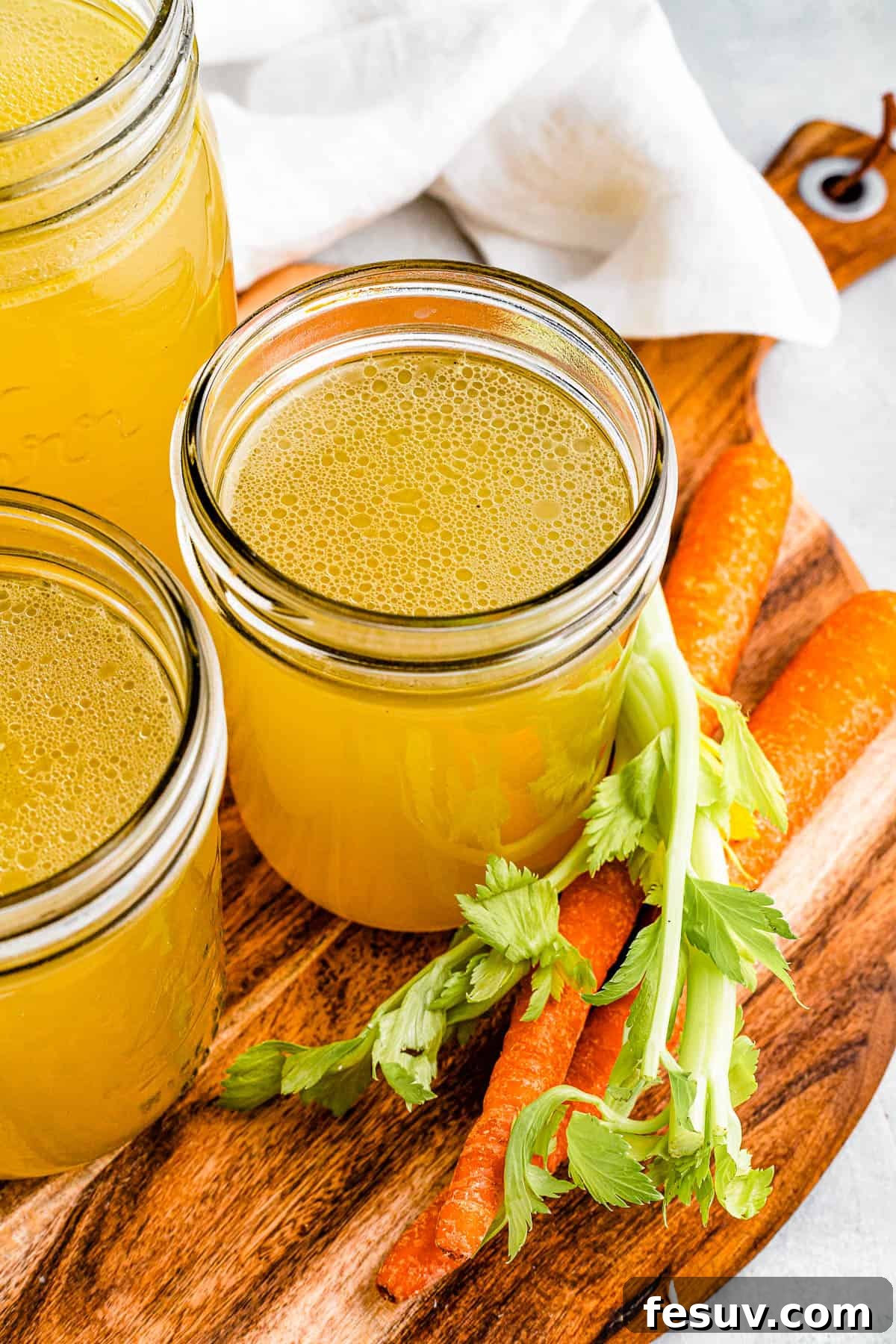 Homemade Instant Pot Chicken Broth 8 Three jars of chicken broth on a cutting board with raw carrots nearby, emphasizing the fresh, homemade quality of the broth.