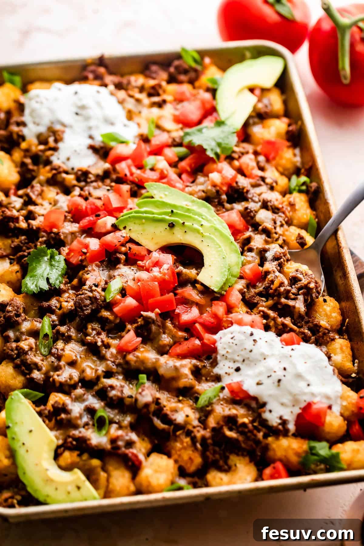 Loaded Sheet Pan Beef Totchos 3 A close-up of sheet pan totchos generously topped with seasoned ground beef, melted cheese, and a vibrant array of fresh toppings like diced tomatoes, sour cream, and sliced avocado.