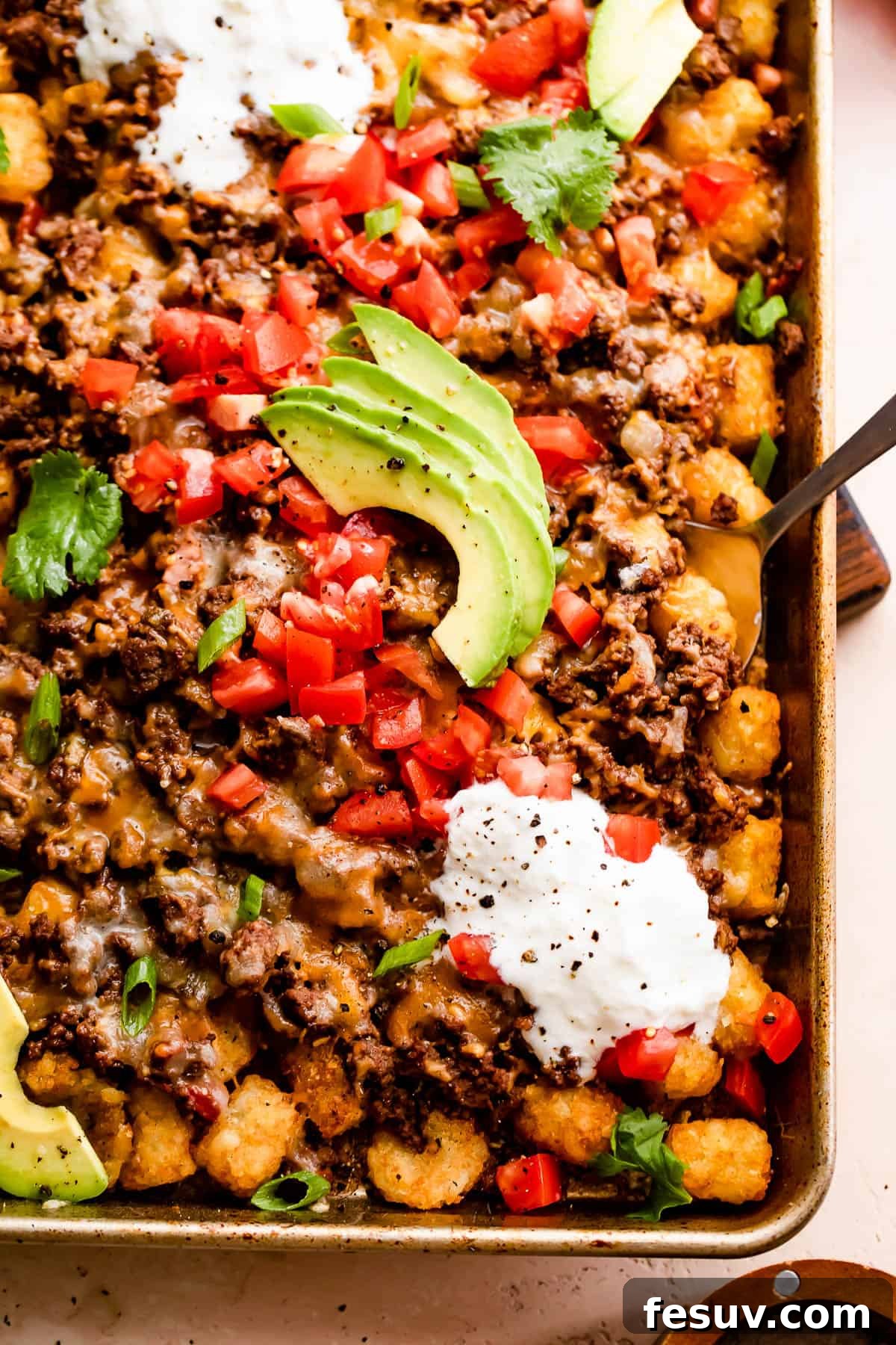 Loaded Sheet Pan Beef Totchos 6 A vibrant and fully loaded sheet pan of totchos, featuring crispy tater tots, seasoned ground beef, melted cheese, fresh tomatoes, sour cream, and sliced avocado, ready for sharing.