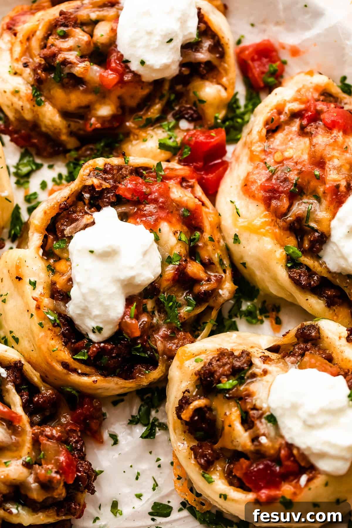 Close-up overhead shot of cooked taco pinwheels topped with fresh diced tomatoes and a dollop of sour cream.