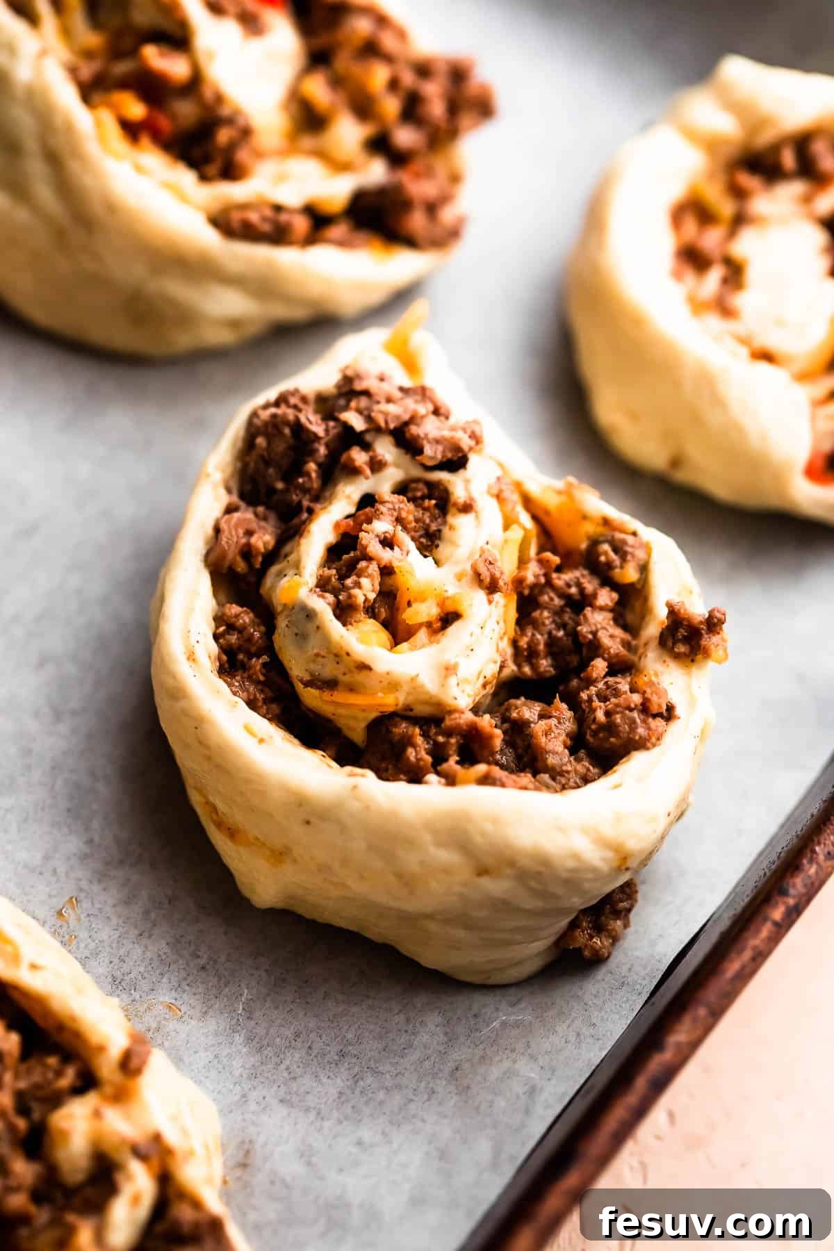 Close-up of ground beef rolled up in pizza dough and neatly cut into individual pinwheels before baking.