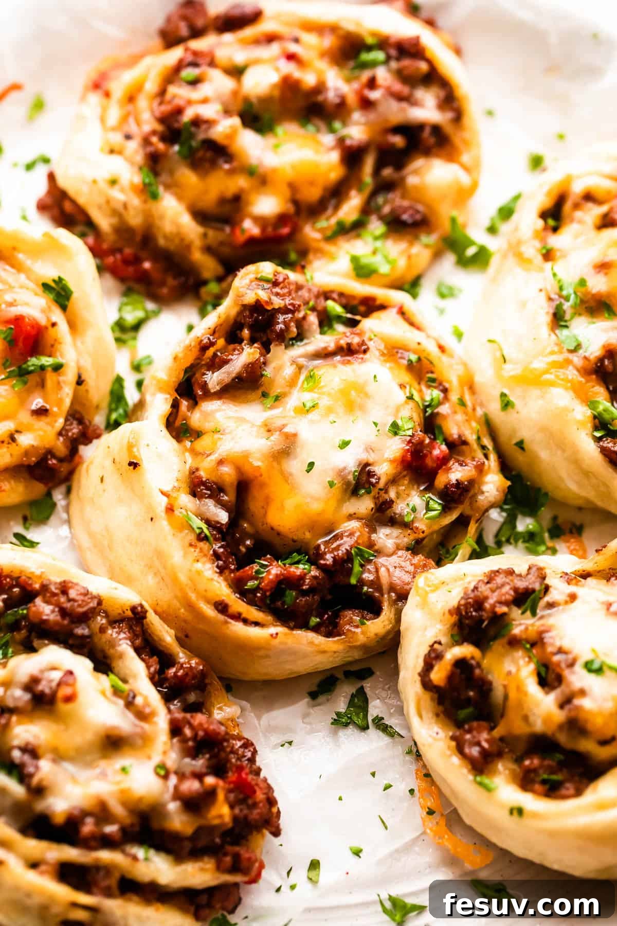 Three golden-brown baked taco pinwheels served on a pristine white background, showcasing their delicious spirals.