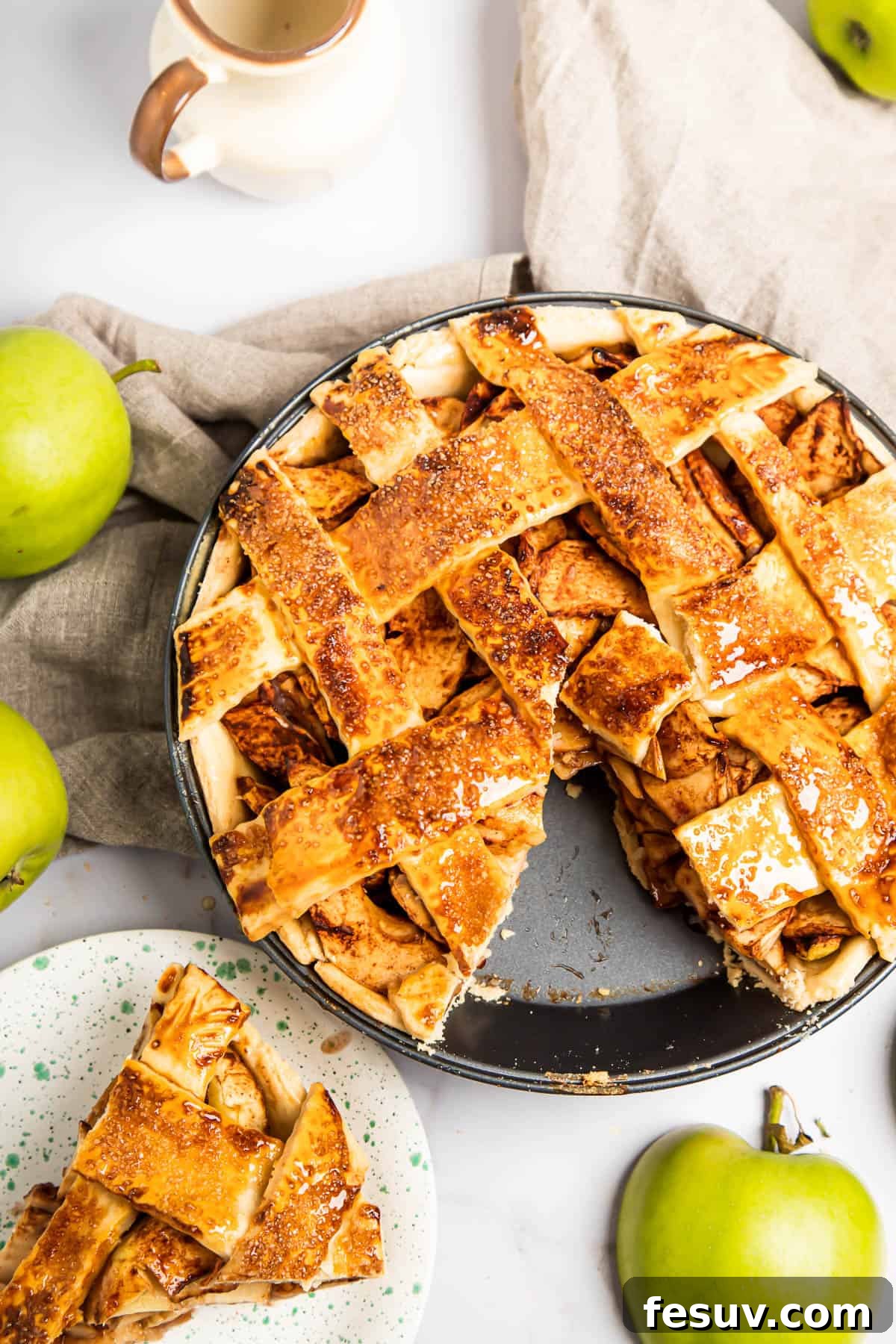 This classic yet easy and delicious Apple Pie recipe is made from scratch, with a buttery, flaky pie crust, fresh apple slices, pie spices, and brown sugar. A baked apple pie with a slice carefully removed and placed on a smaller saucer nearby, showcasing the rich apple filling and flaky crust.